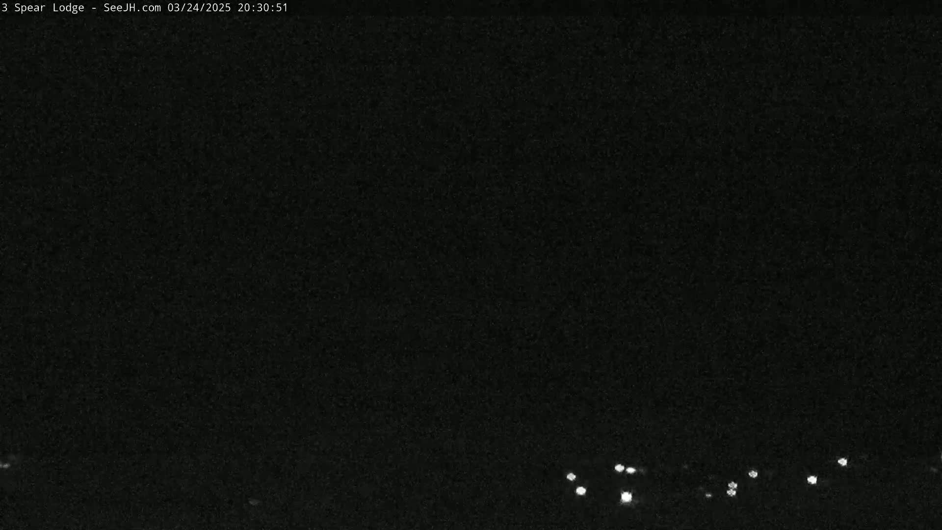 A nighttime, low-light image shows a few small, distant lights at the bottom of the frame against a dark, mostly featureless background.