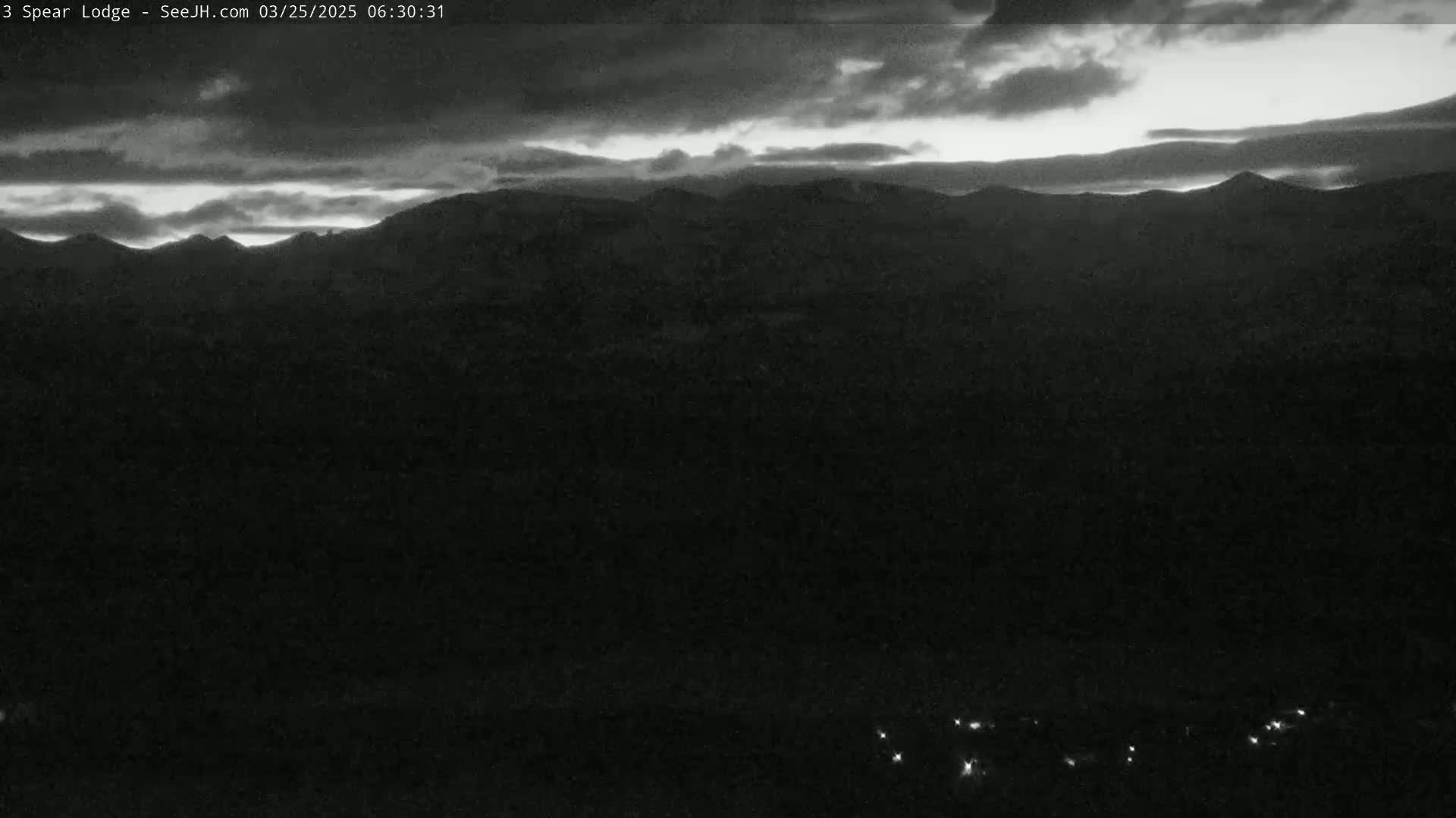 A dark, overcast sky over a silhouetted mountain range with a few faint lights visible in the distance.