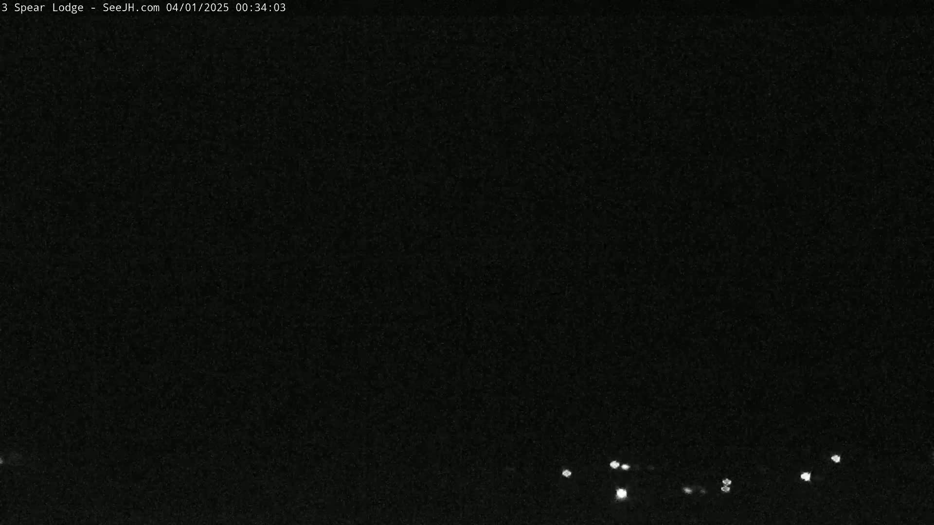 A nighttime, dark outdoor scene shows a few small, distant lights at the bottom of the frame.