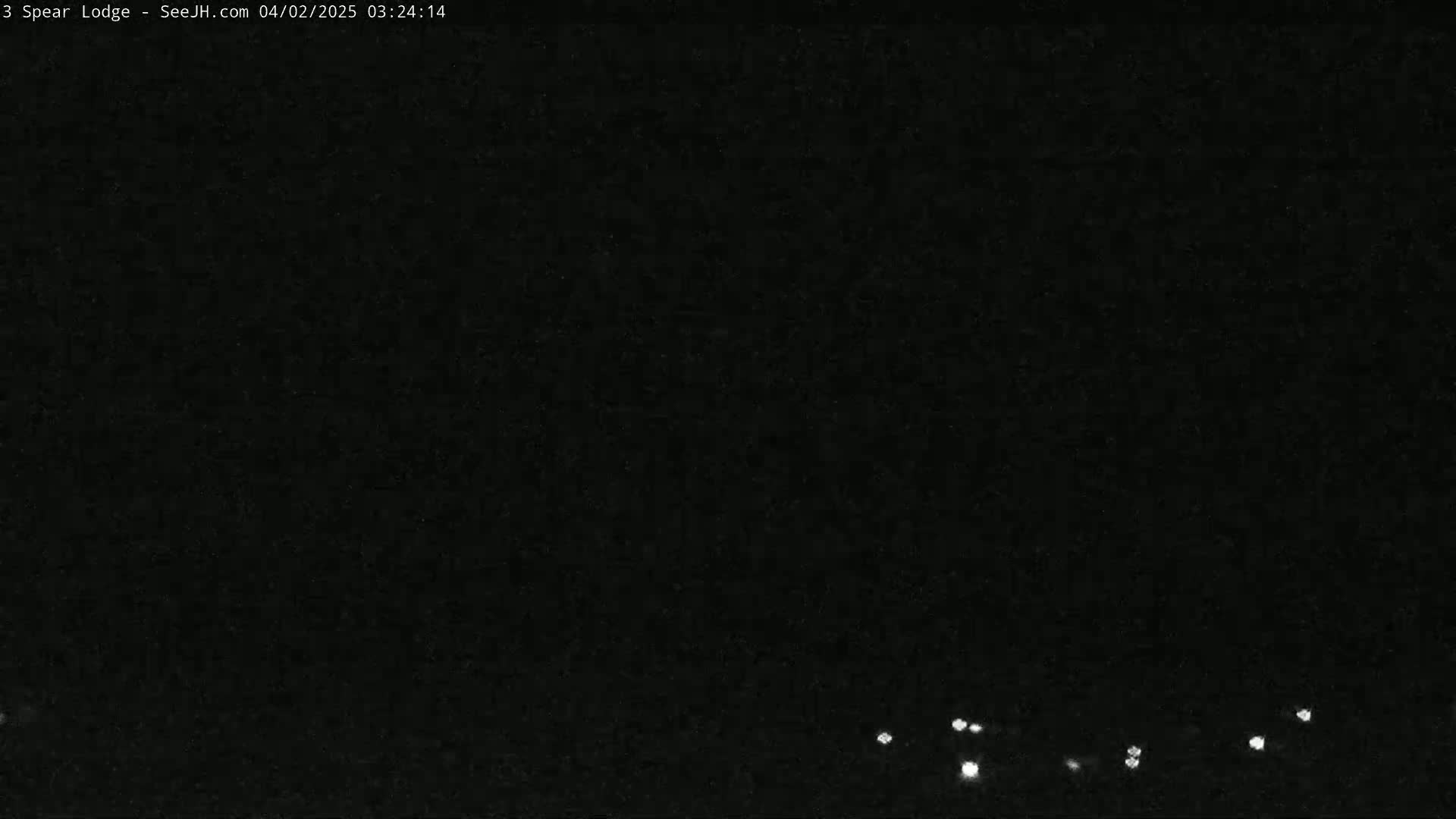 A dark, nighttime scene shows a few faint lights on the horizon under a clear, black sky.
