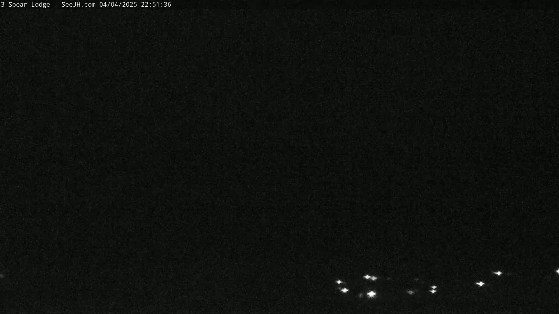 A nighttime, dark image shows a low horizon line with several small, bright lights in the distance.