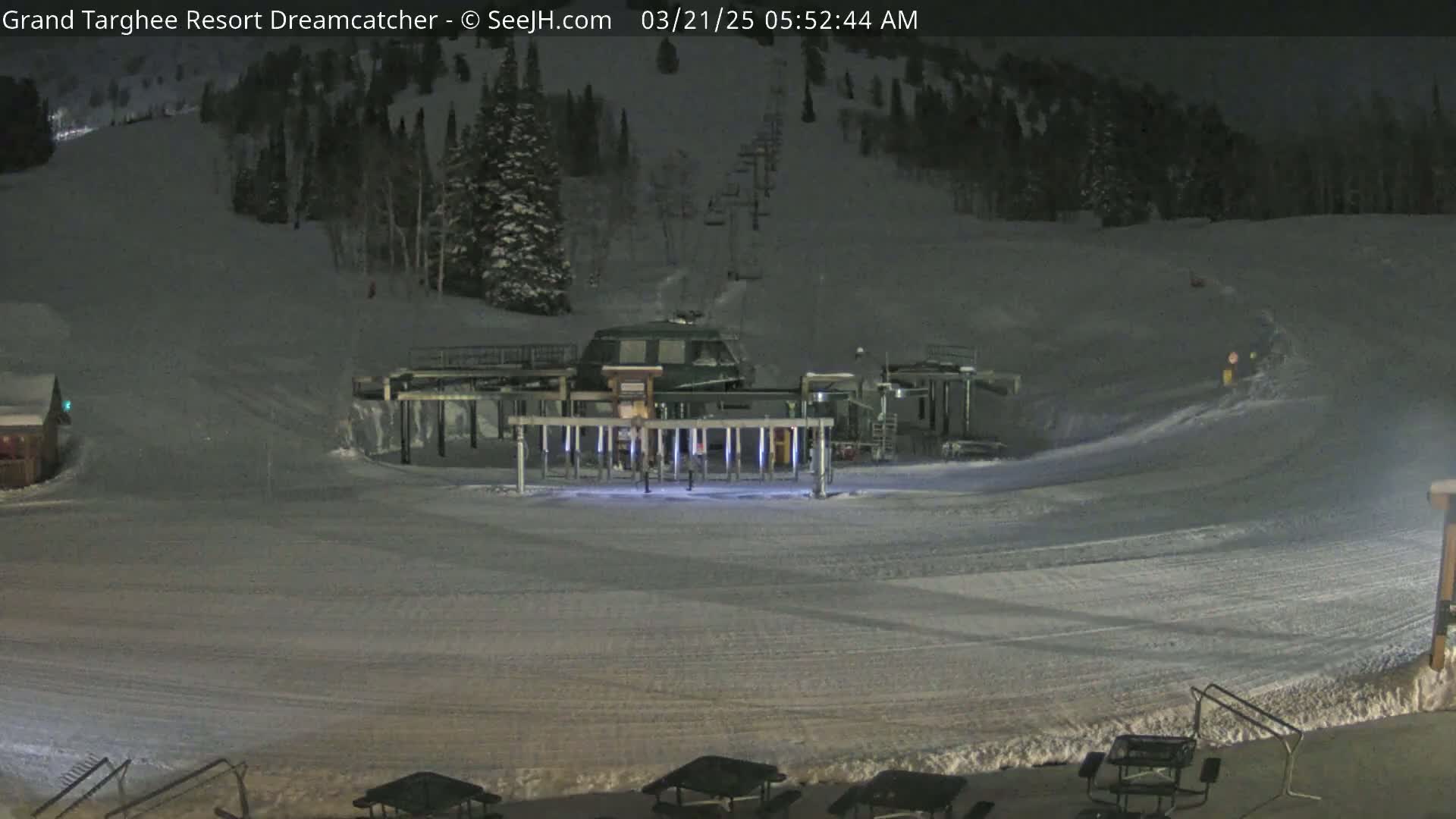 A nighttime view of a snow-covered ski slope with a chairlift station and several picnic tables in the foreground.