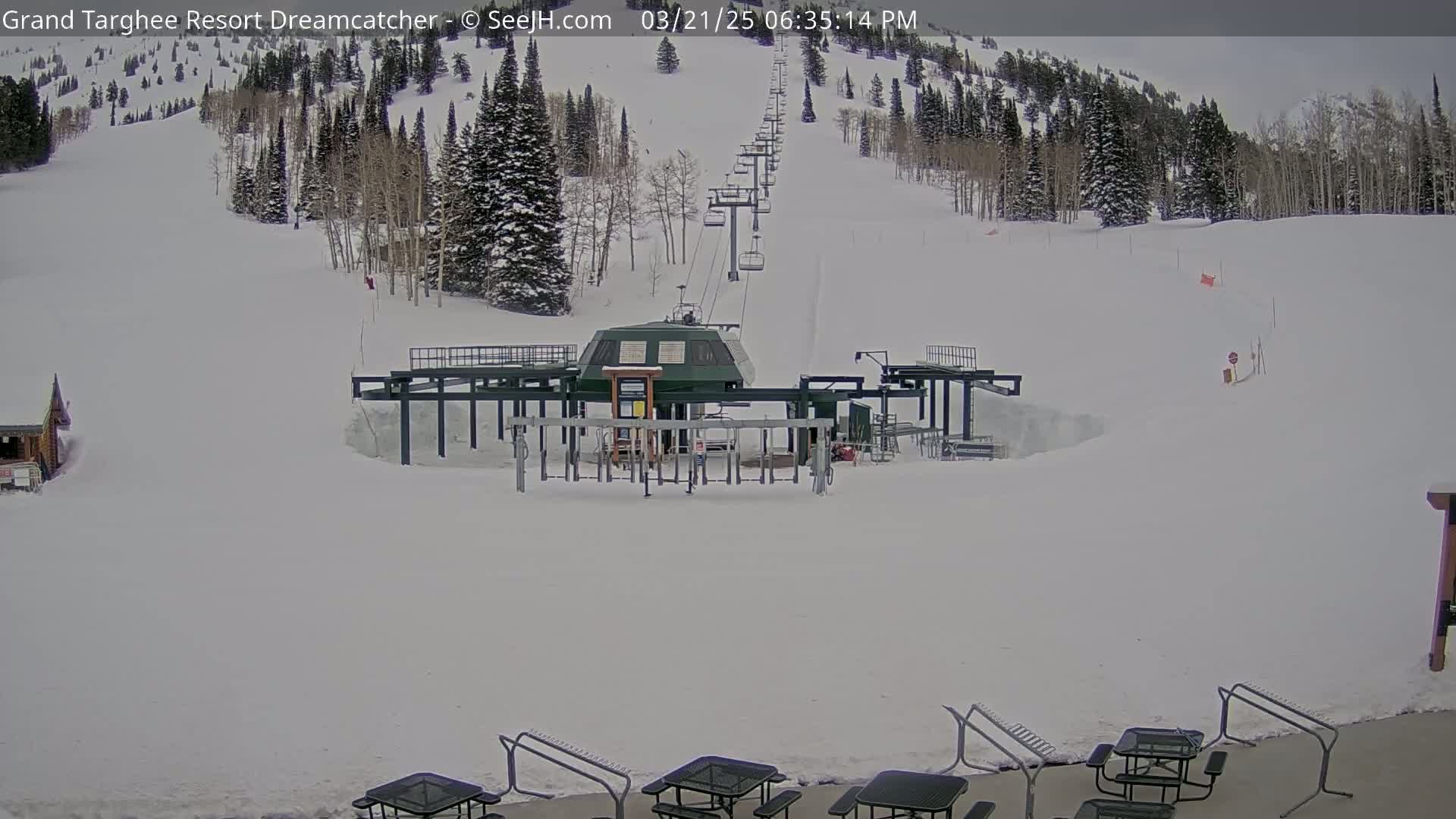 A ski lift base station sits in a snowy landscape, with a chairlift ascending a snow-covered mountainside under an overcast sky.