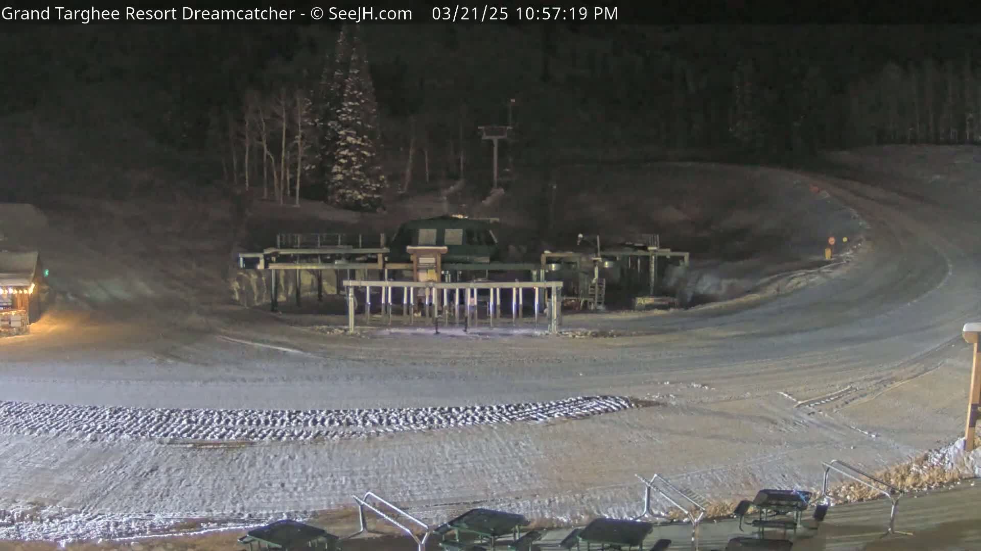 A snow-covered ski resort at night, showing a ski lift and a gently curving ski run.