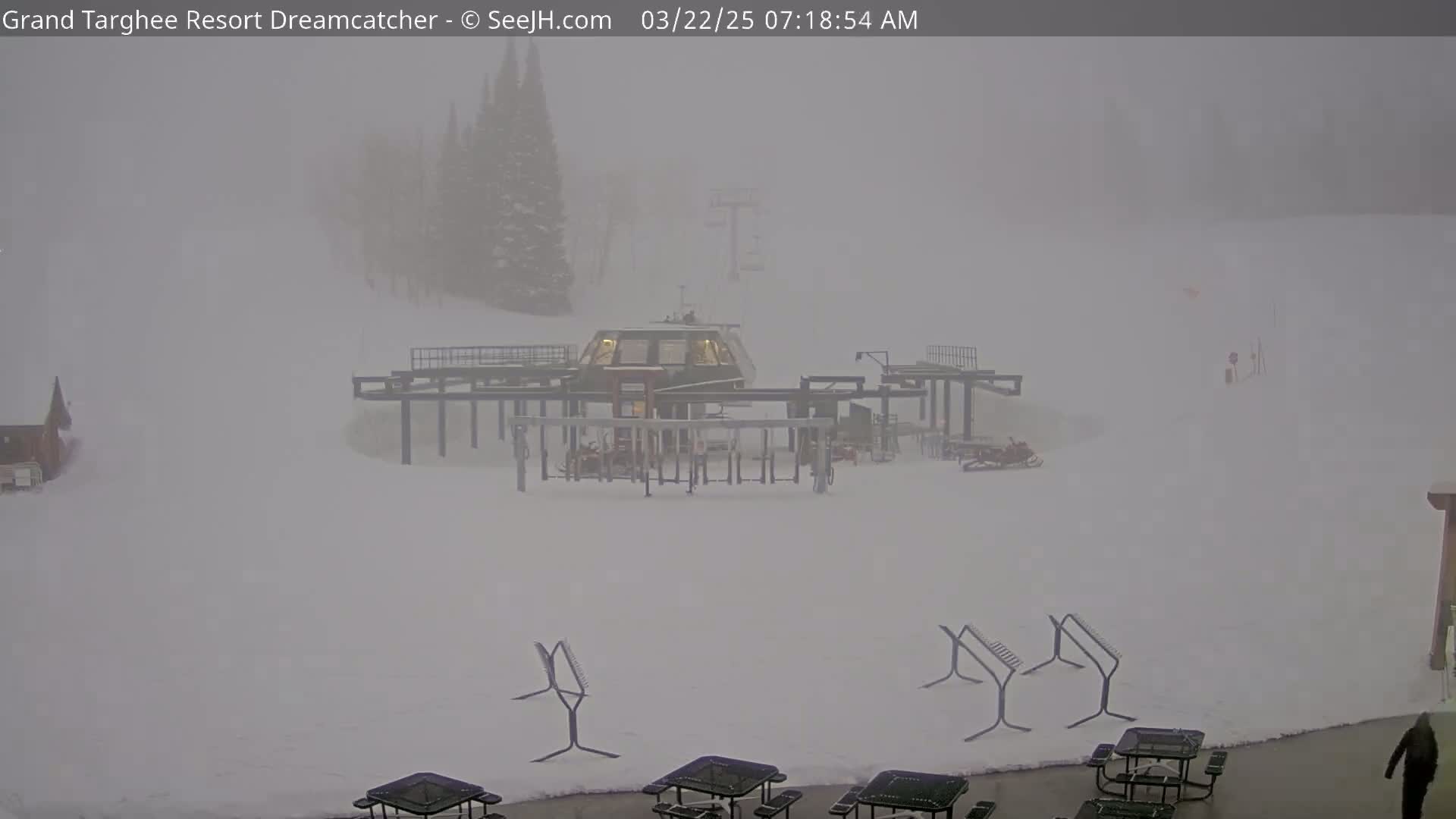 A snow-covered ski lift base area is shrouded in heavy fog.