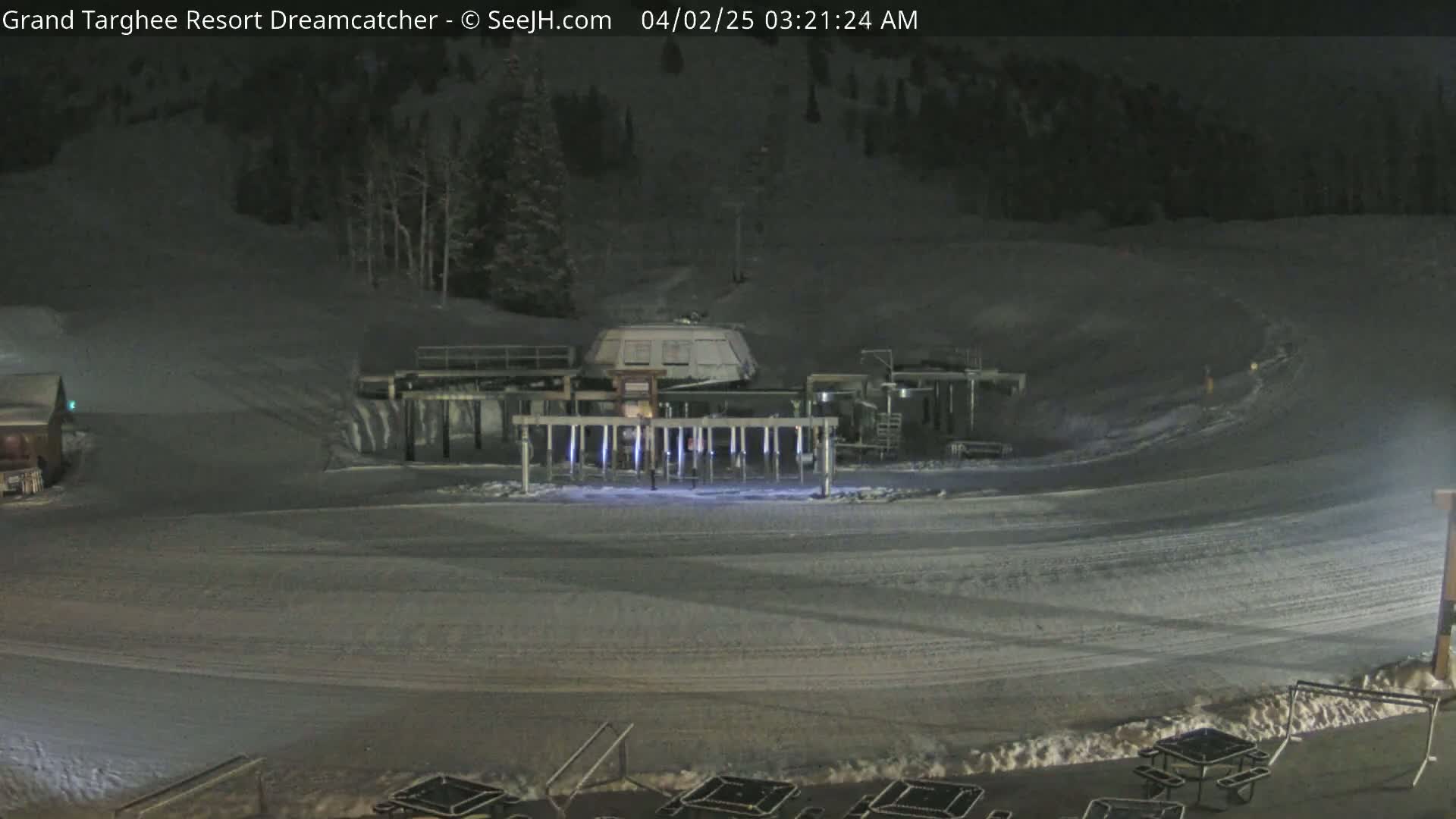 A snow-covered ski lift base area is illuminated at night.