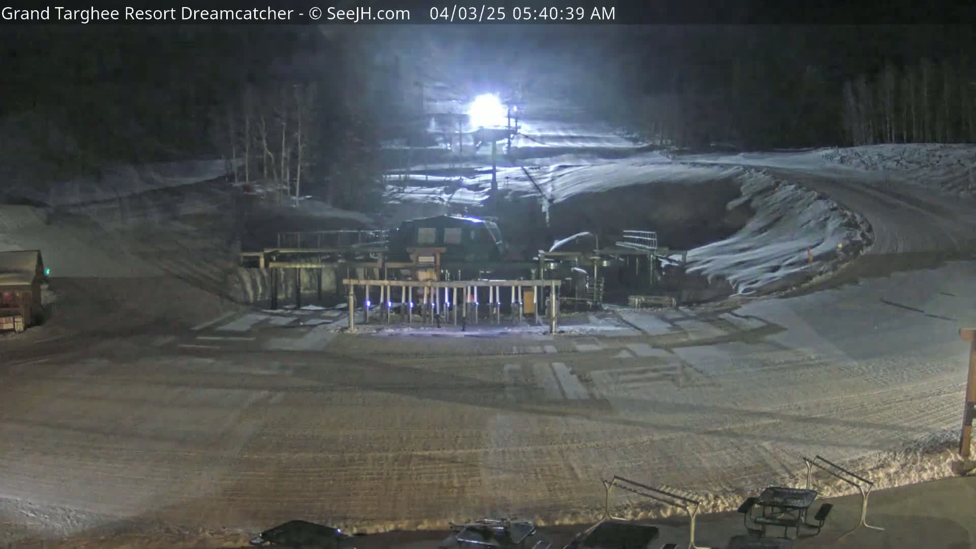 A nighttime view of a snow-covered ski resort slope with a ski lift in the center, illuminated by artificial lights.