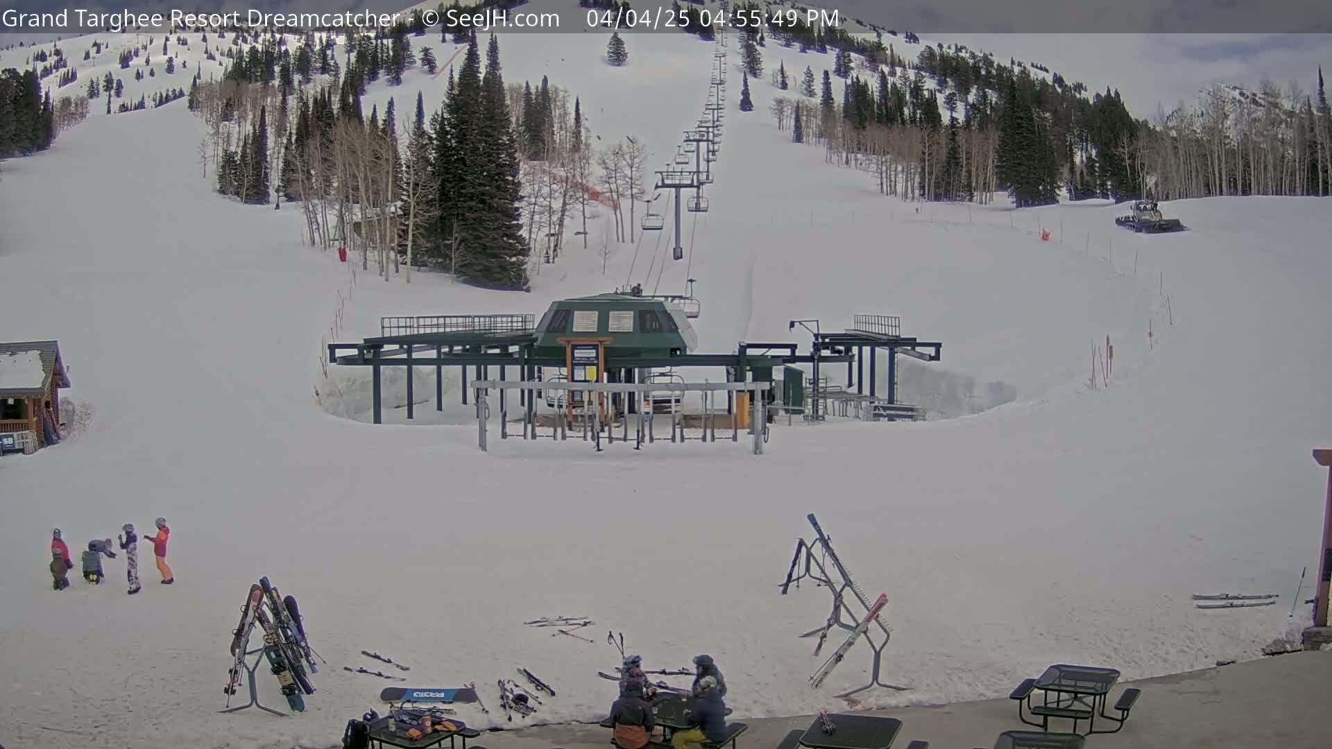 A ski lift base area with snow-covered slopes and mountains in the background under a partly cloudy sky.