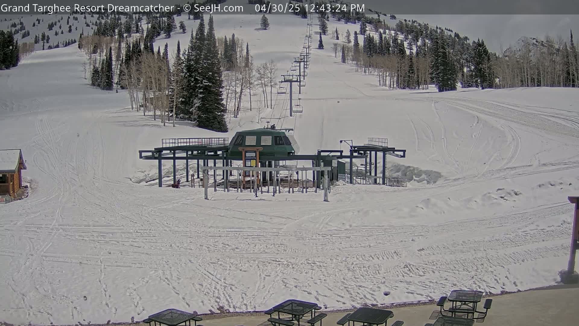 A ski lift base station sits at the bottom of a snow-covered ski slope on a partly cloudy day.