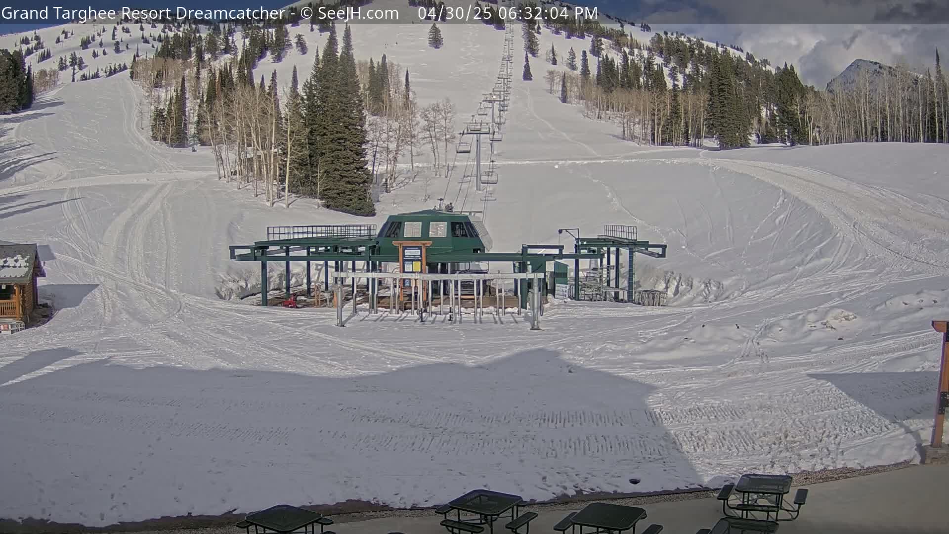 A ski lift base station sits at the bottom of a snow-covered ski slope on a partly sunny day.