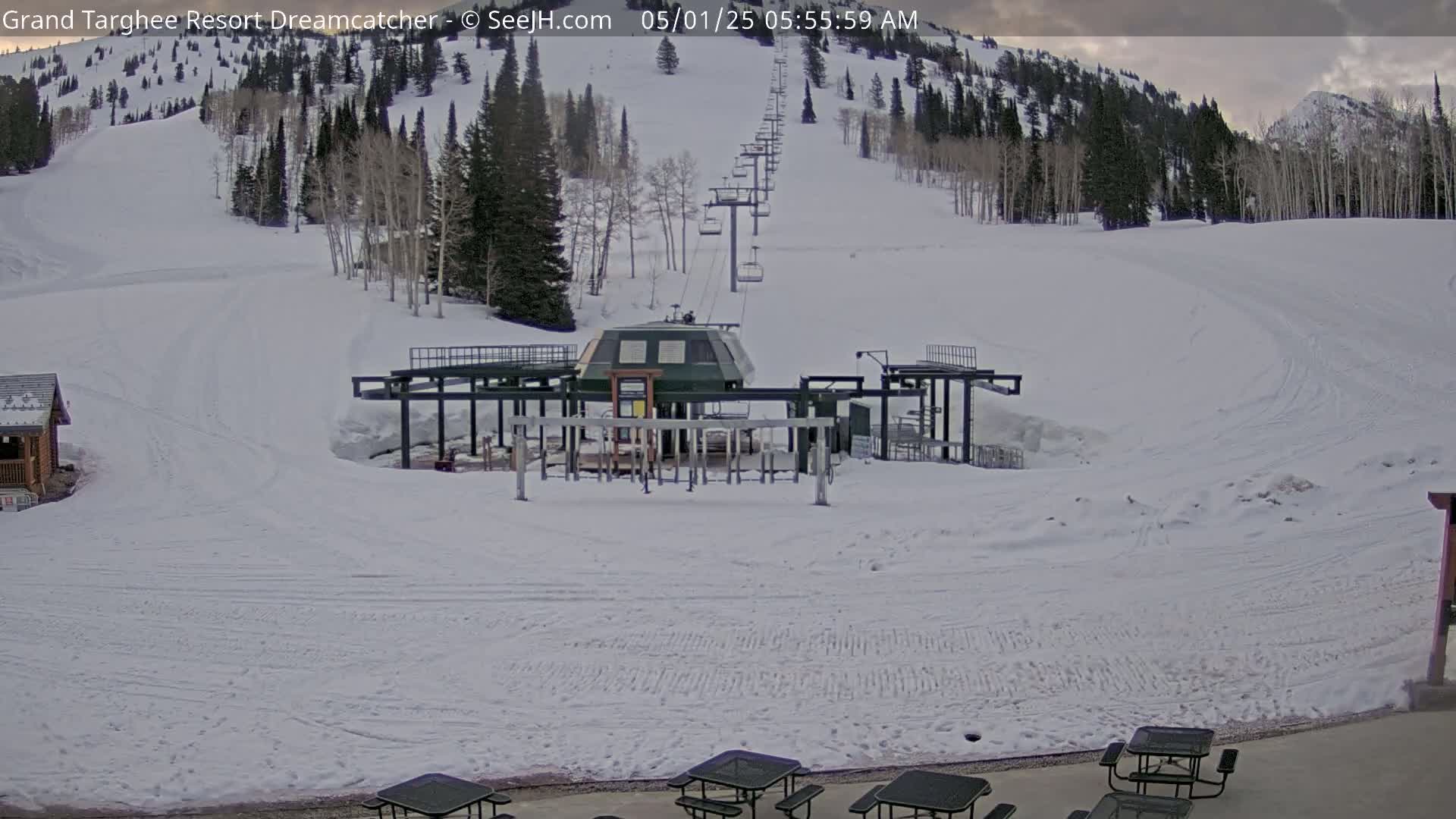 A ski lift base station sits at the bottom of a snow-covered ski slope on a cloudy morning.