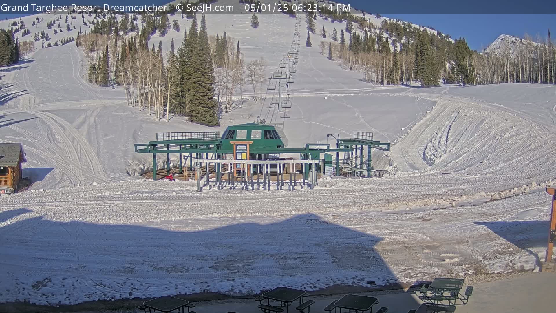 A ski lift base station sits in a snowy mountain landscape under a sunny sky.