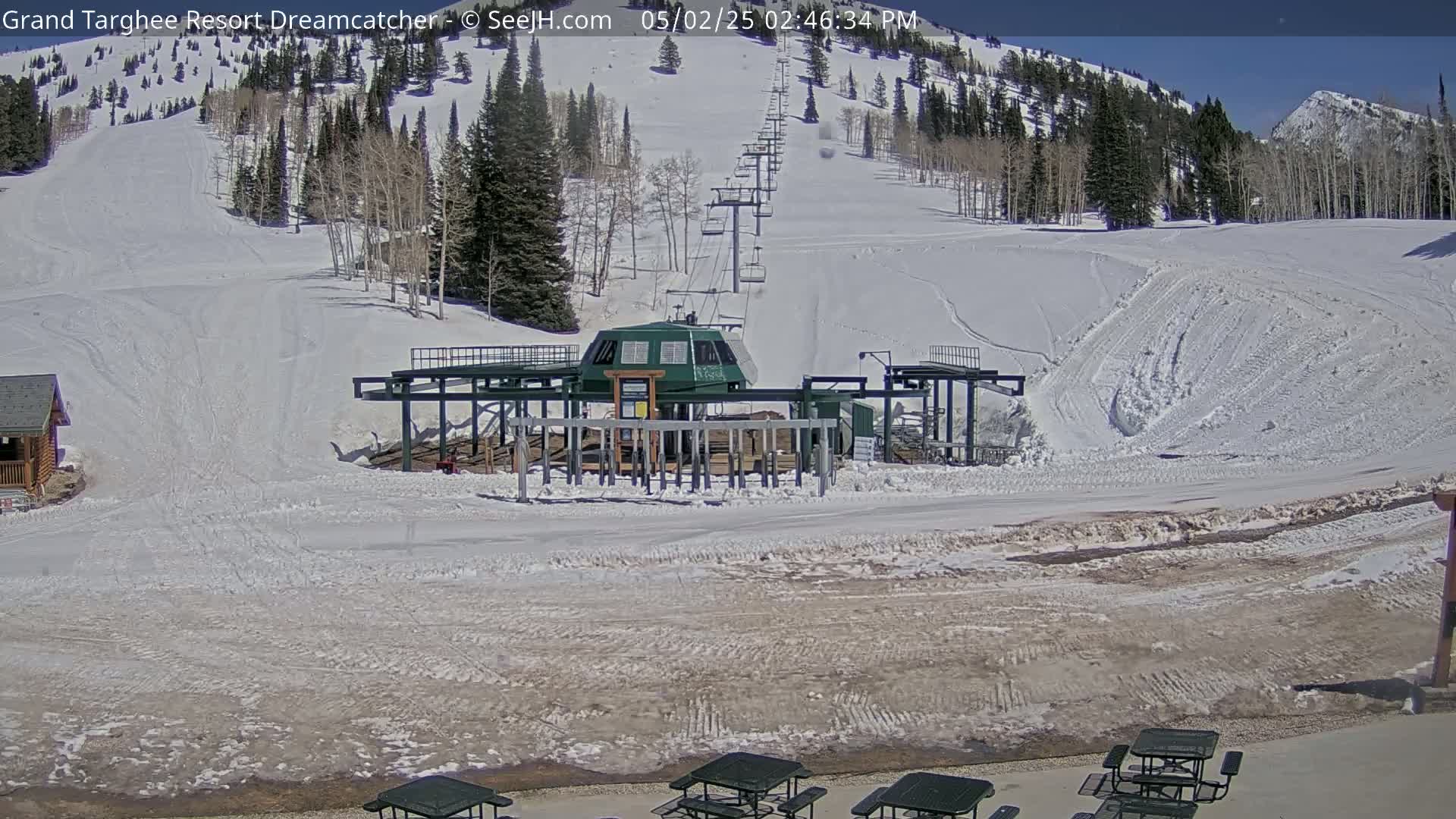 A snow-covered ski slope with a chairlift and several picnic tables sits under a sunny sky.