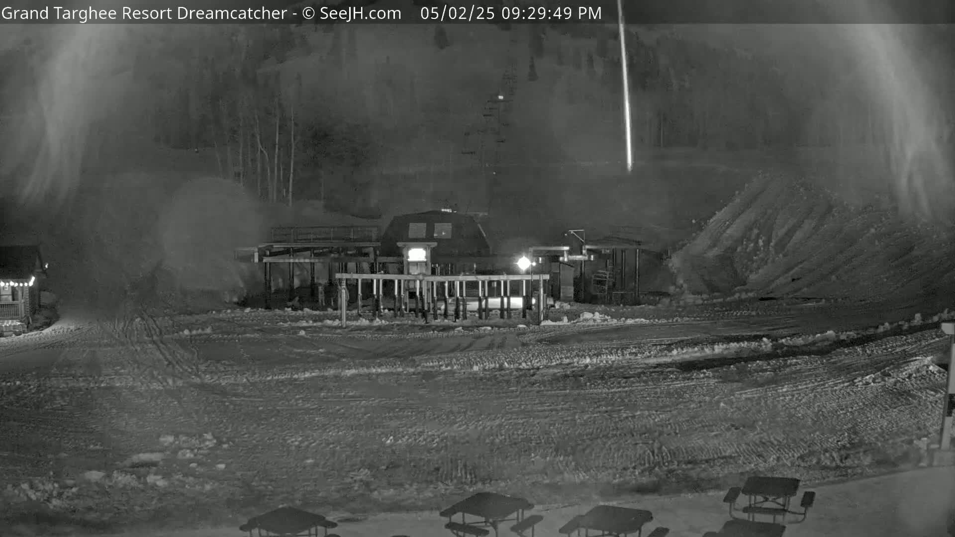 A nighttime snow scene shows a ski lift station with snow blowing around it, and picnic tables in the foreground under a dark, snowy sky.
