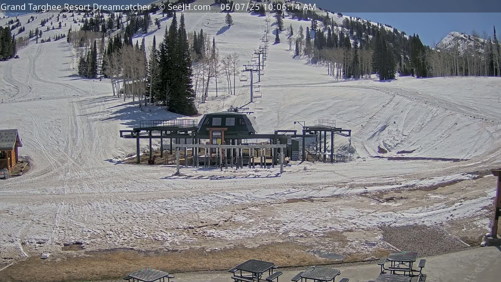 A ski lift base station sits at the bottom of a snow-covered ski slope on a sunny day.