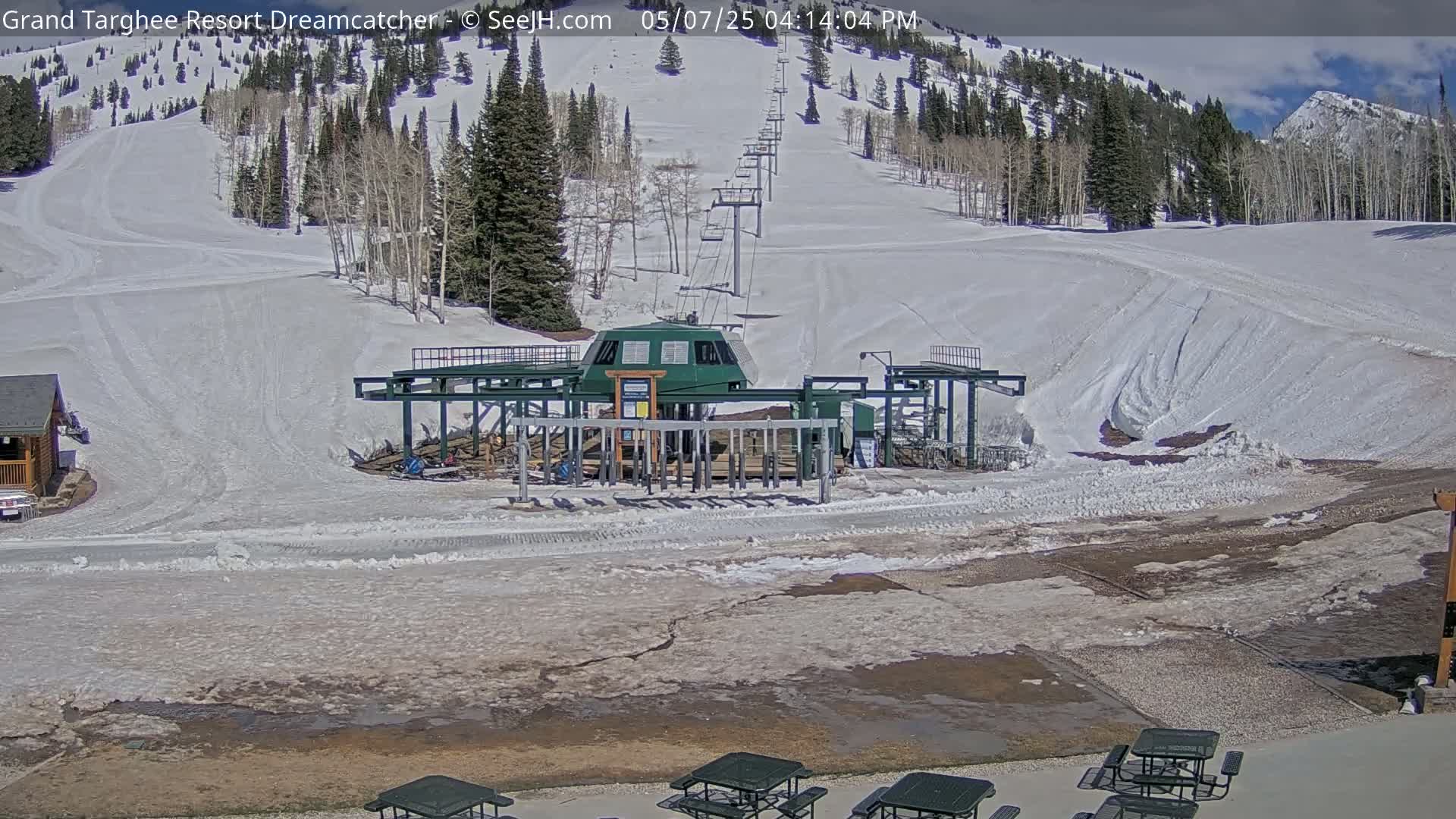 A ski lift base station sits at the bottom of a snow-covered ski slope on a partly sunny day.