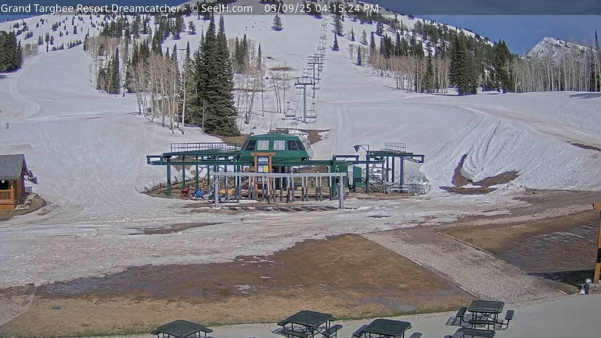 A ski lift base station sits in a mostly snow-covered area at the base of a mountain on a partly sunny day.