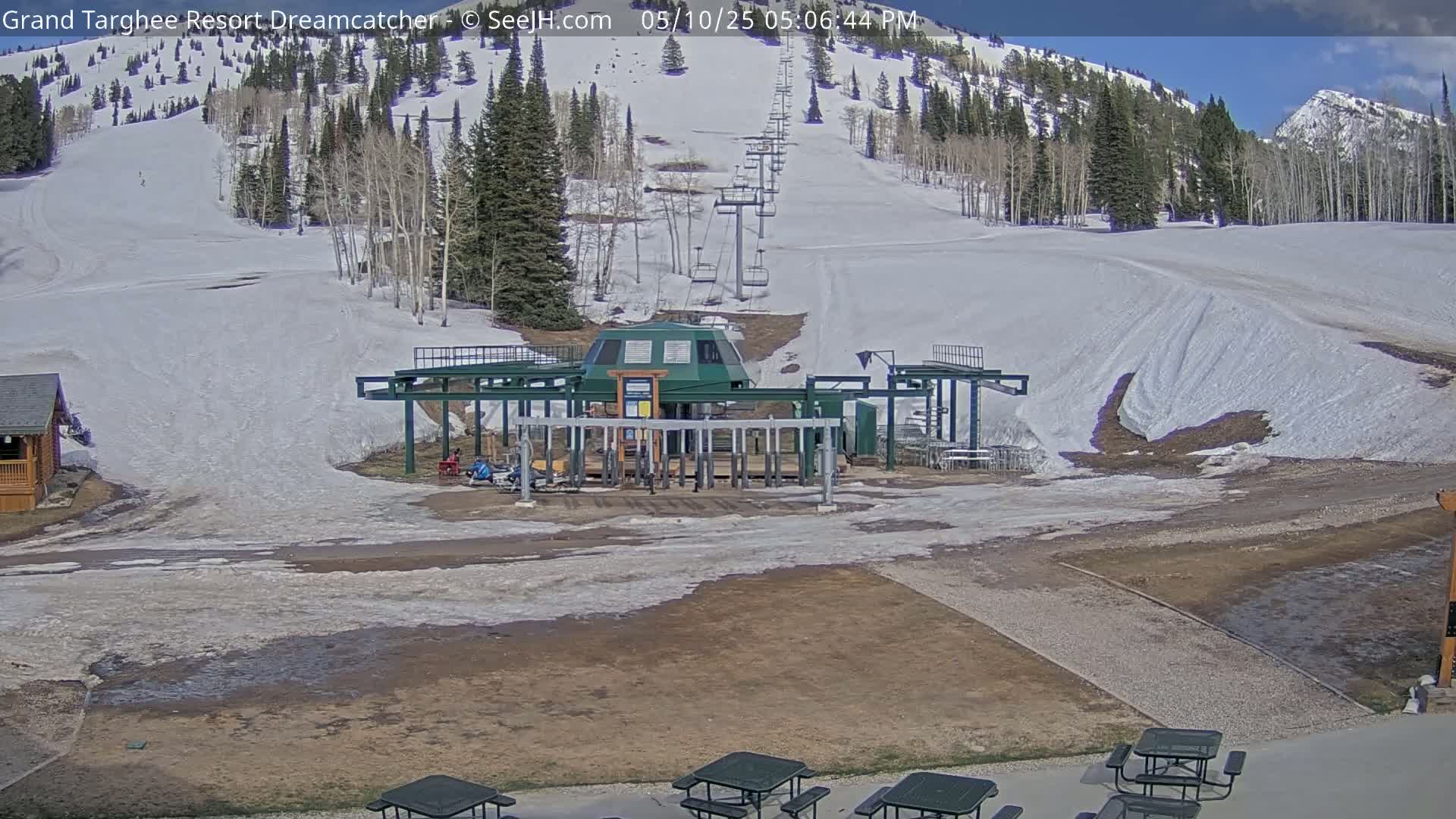 A ski lift base station sits in front of a snow-covered ski slope on a partly sunny day.