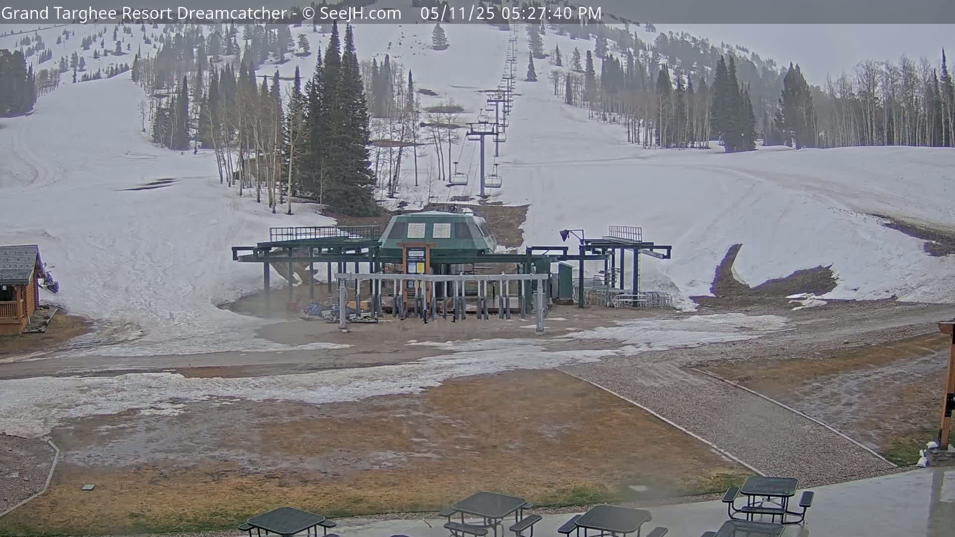 A chairlift base station sits at the bottom of a snow-covered ski slope on an overcast day.