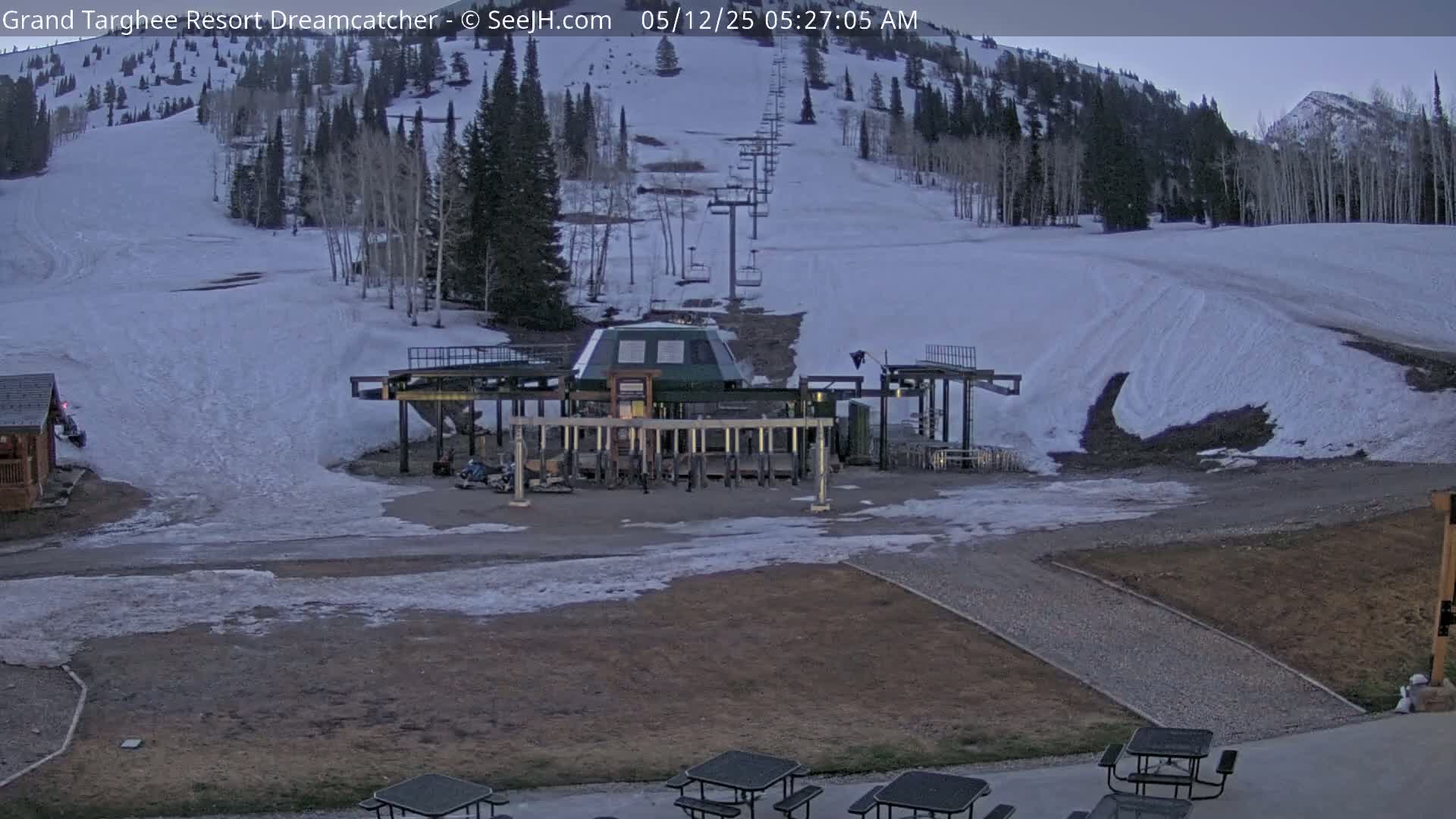 A ski lift base station sits at the bottom of a snow-covered ski slope on a mostly clear morning.