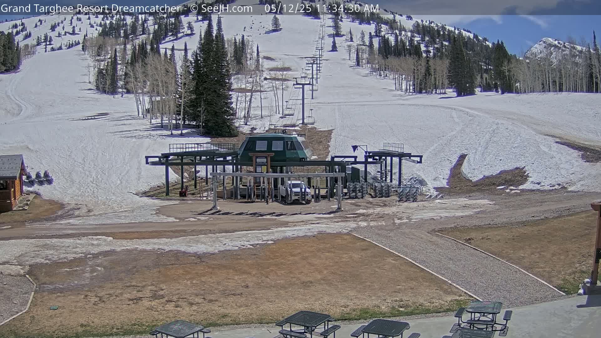 A ski lift base station sits in a mostly sunny, snow-covered mountain setting.