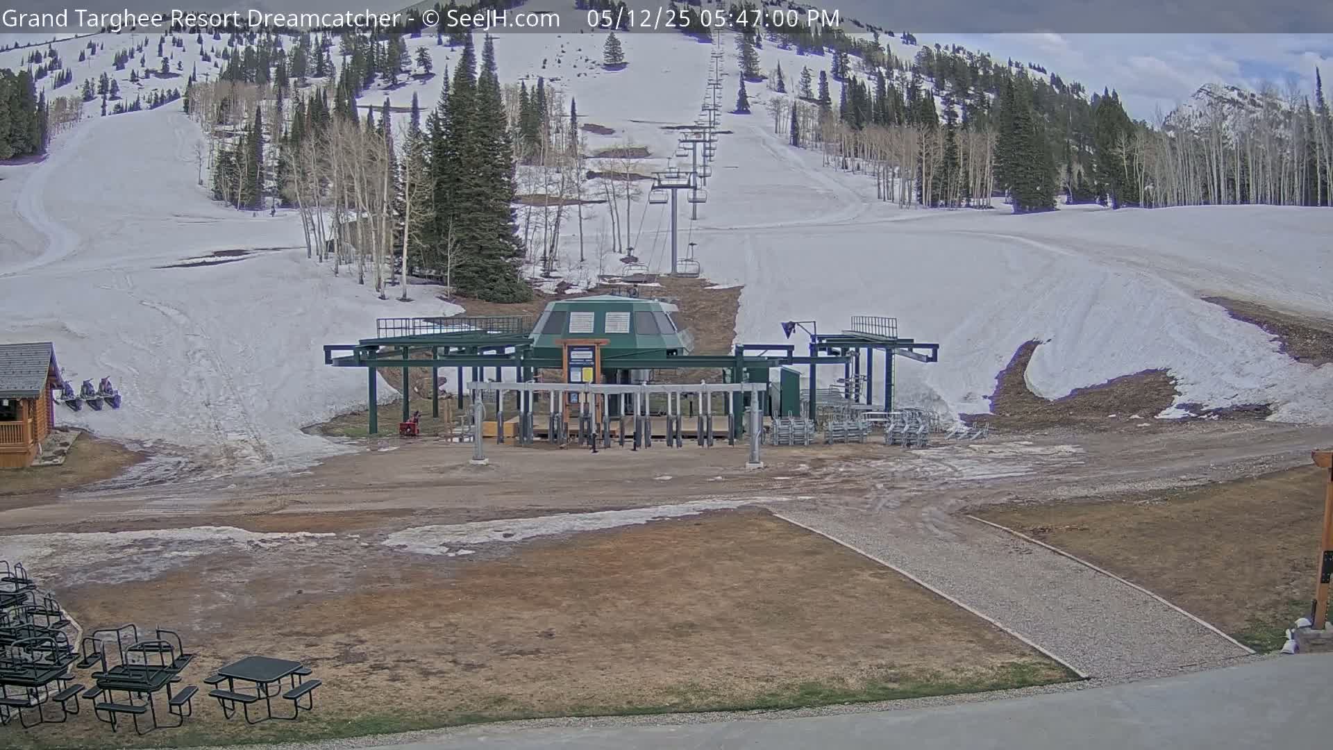 A ski lift base station sits at the bottom of a snow-covered ski slope, with partially cloudy skies overhead.