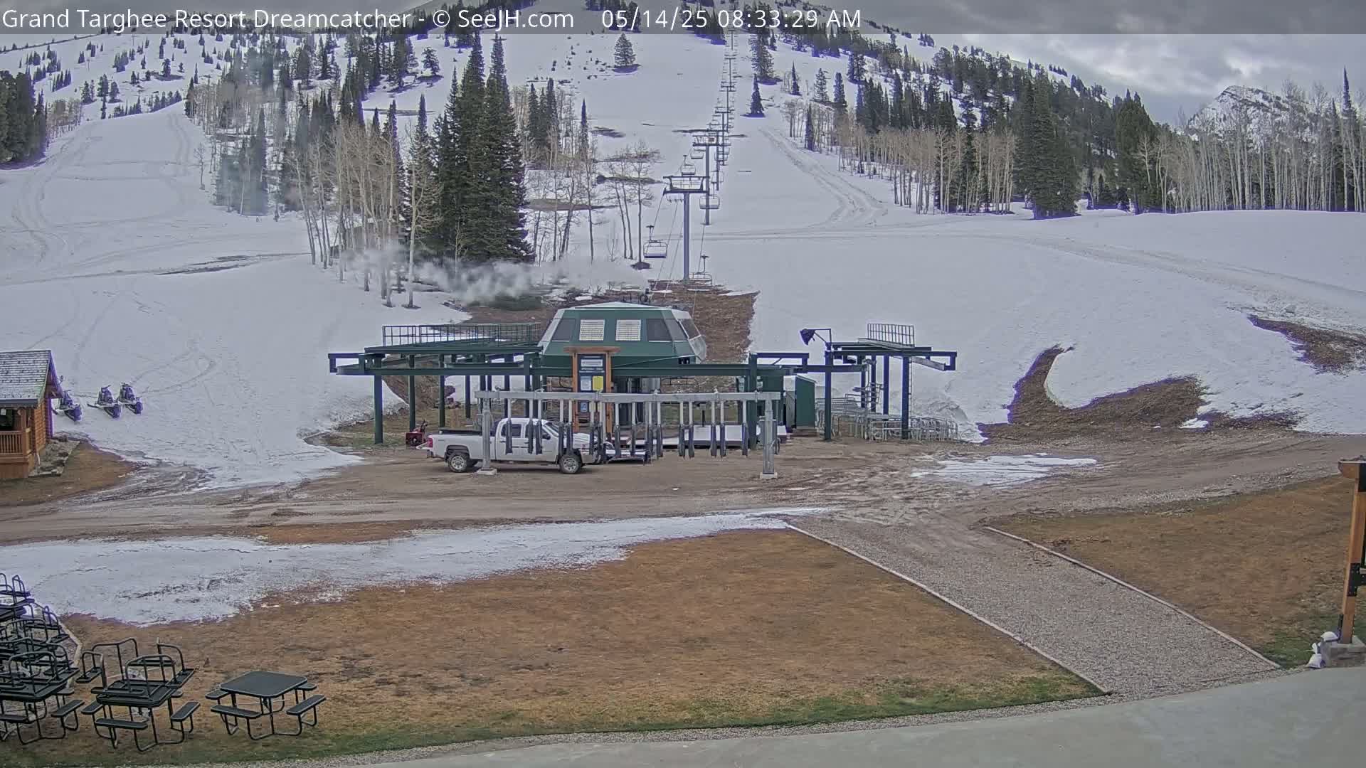 A ski lift base station sits at the bottom of a snow-covered ski slope on an overcast day, with several snowmobiles parked nearby.