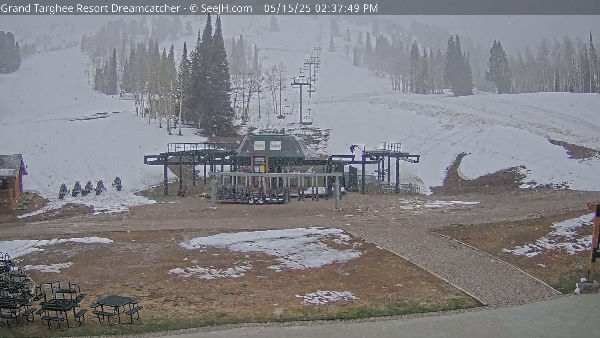 A ski lift base area with snow-covered slopes and light snowfall is visible, with several snowmobiles parked nearby.