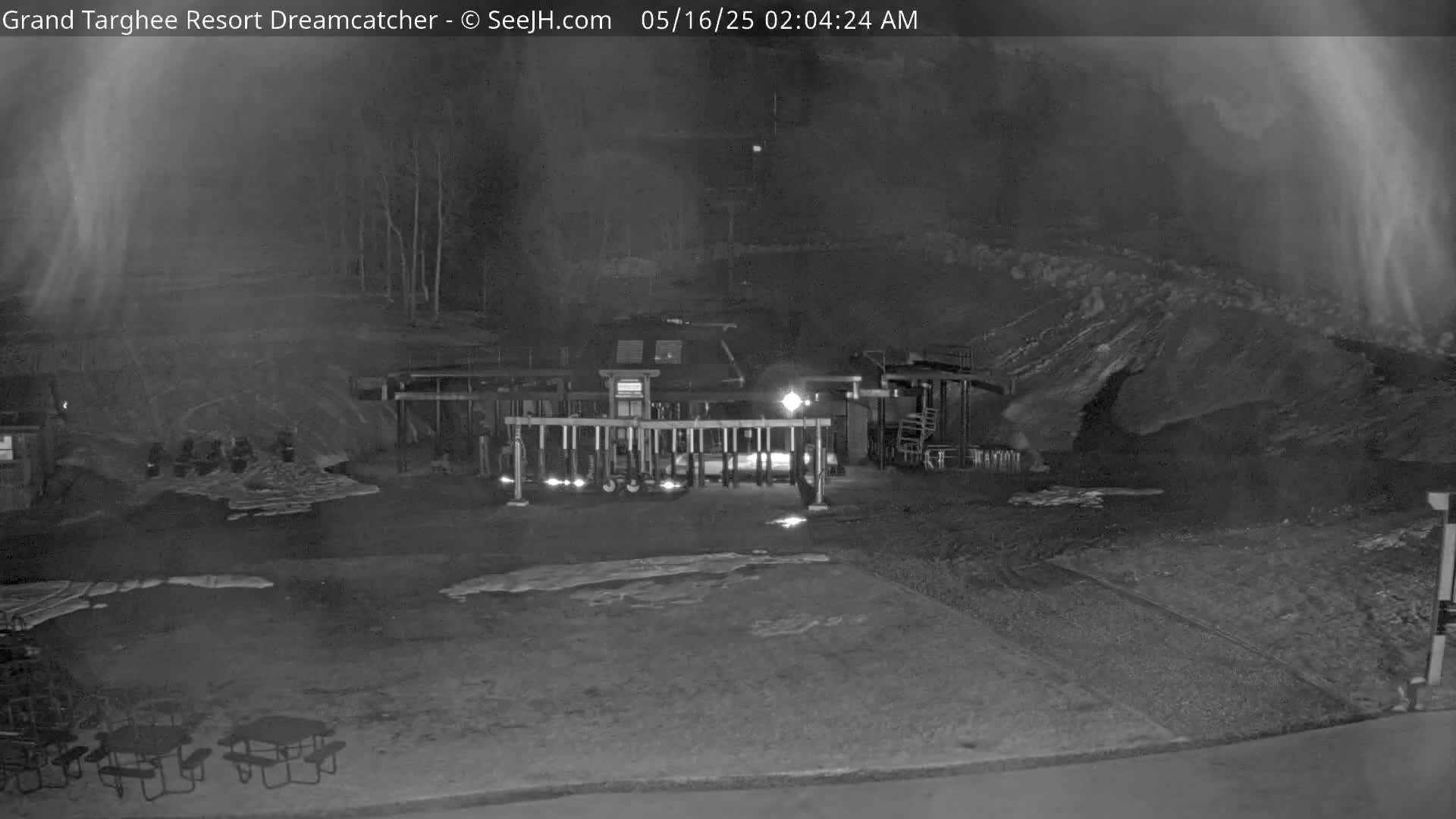 A nighttime, low-light view of a gated area with several picnic tables and a building, possibly a resort, under foggy conditions.