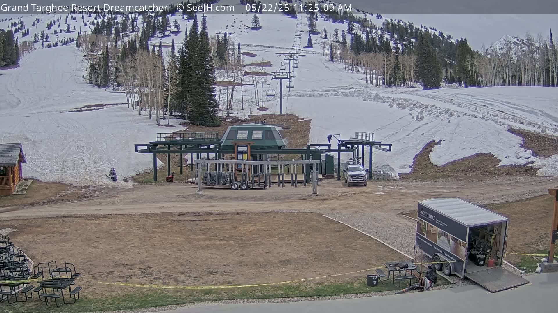 A ski lift base station sits near a mostly snow-covered ski slope, under a partly cloudy sky.