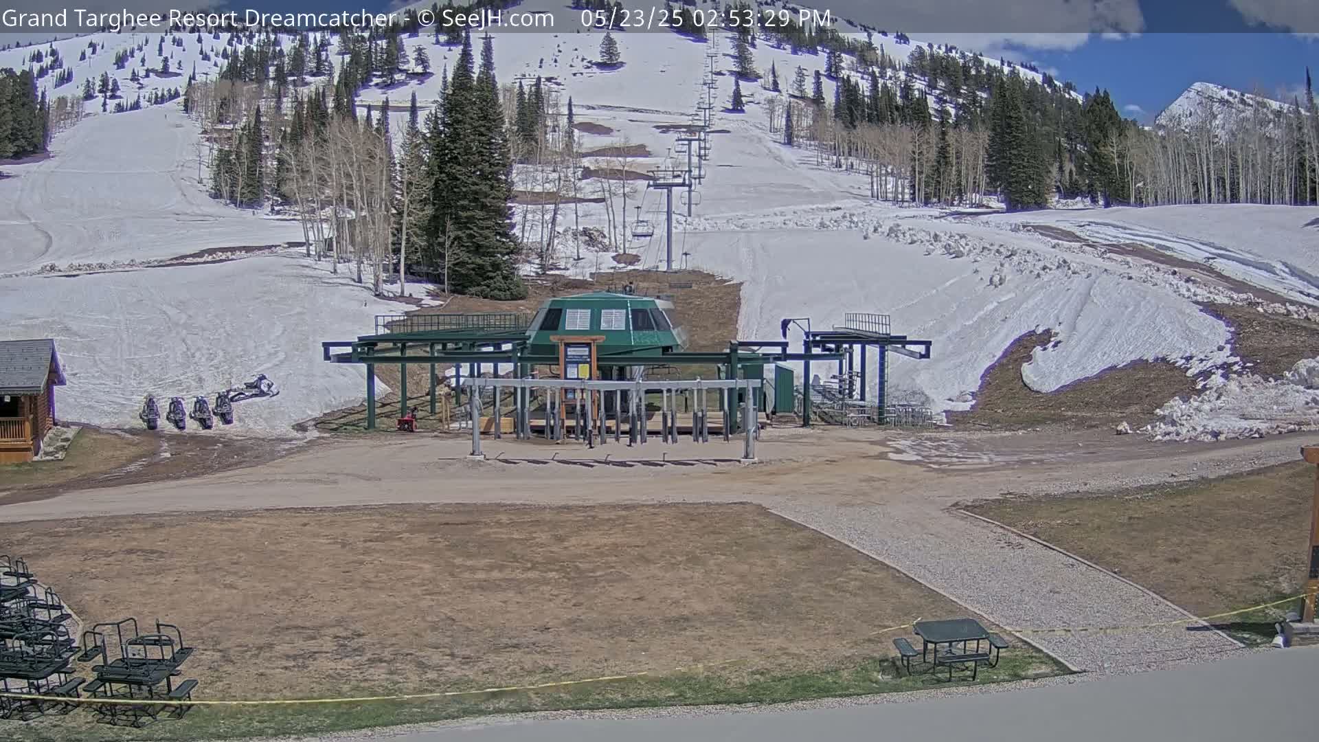 A ski lift base station sits in a partially snow-covered mountain landscape under a partly sunny sky.