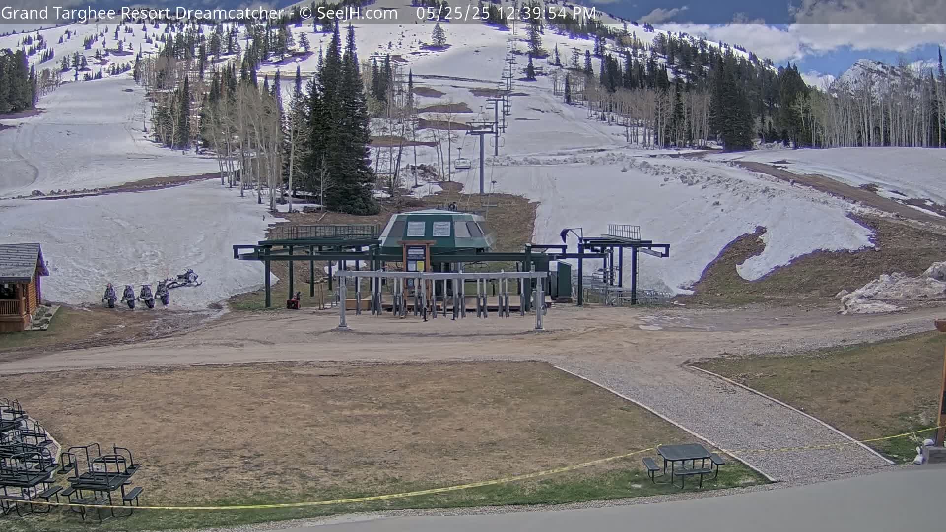 A ski lift base station sits in a mostly snow-free area at the base of a snow-covered mountain under a partly sunny sky.