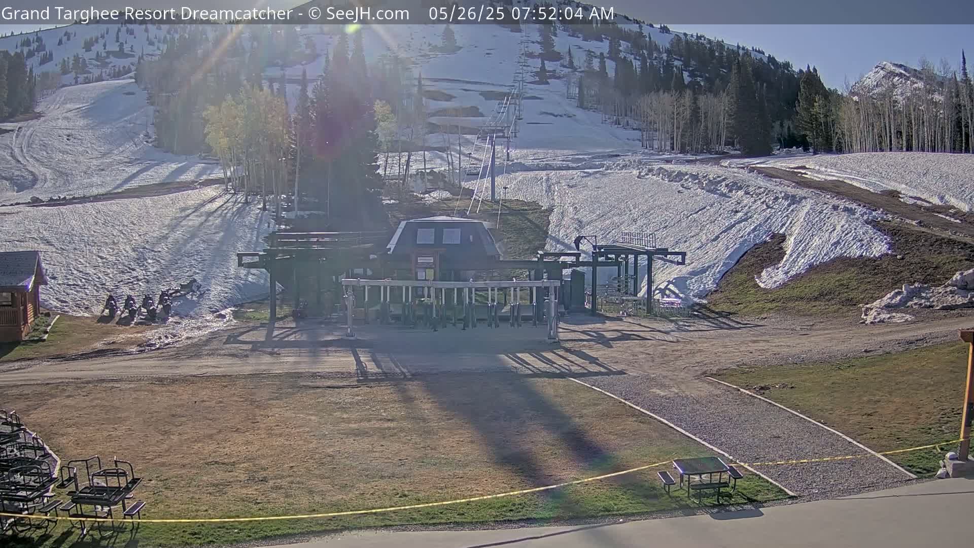 A ski lift base station sits at the bottom of a snow-covered ski slope on a sunny morning.