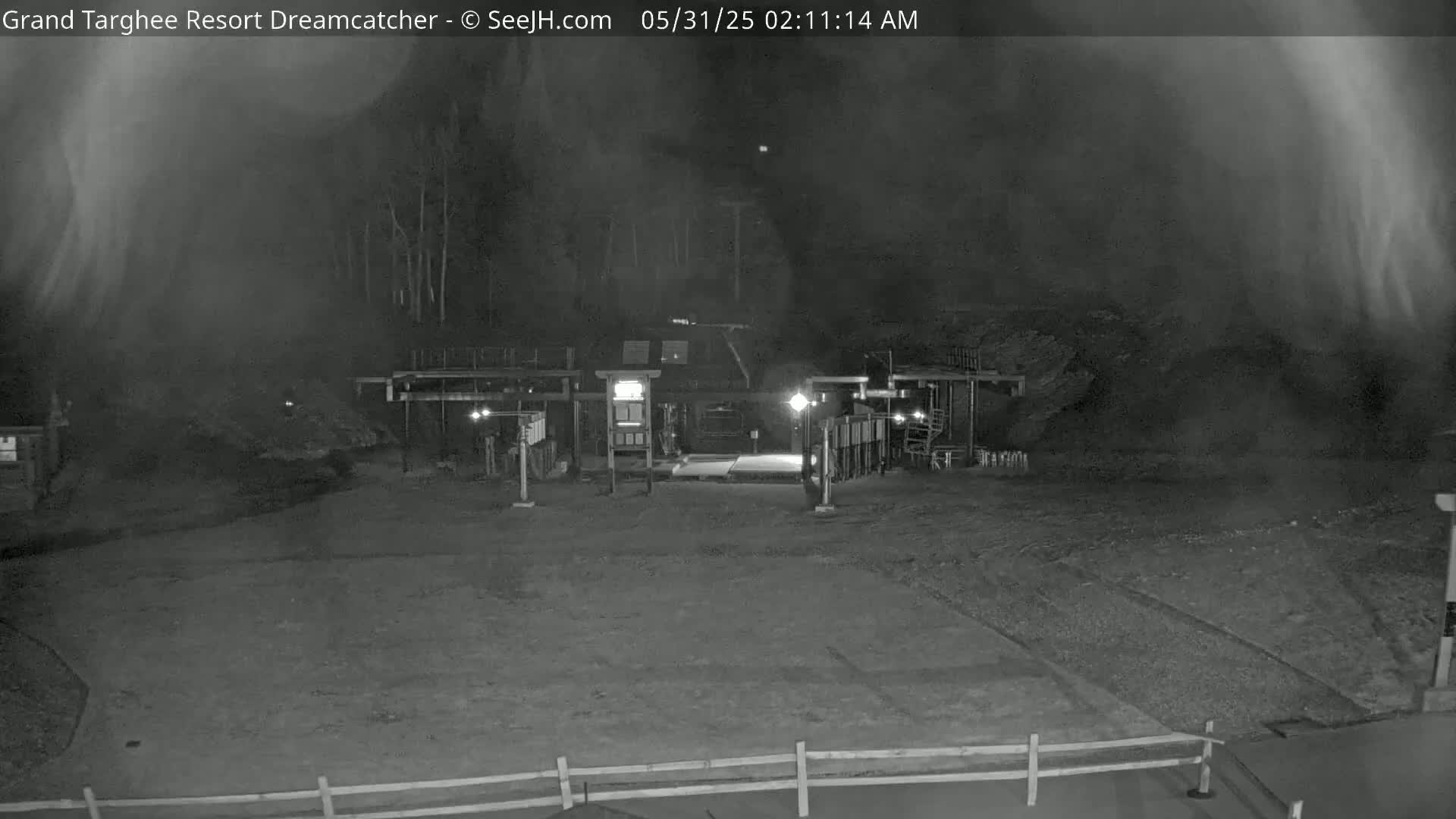 A nighttime view of a mostly empty, dimly lit area in front of a building, with hazy or foggy conditions present.