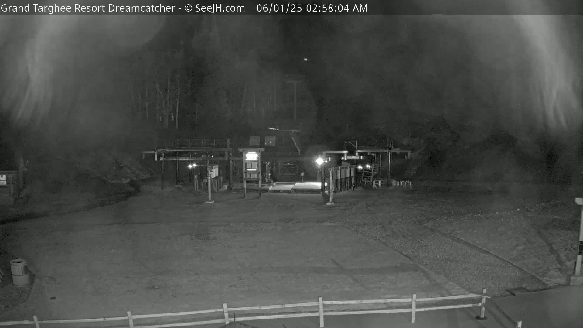 A nighttime, foggy view of a building with lights and a gated entrance, possibly a ski resort.