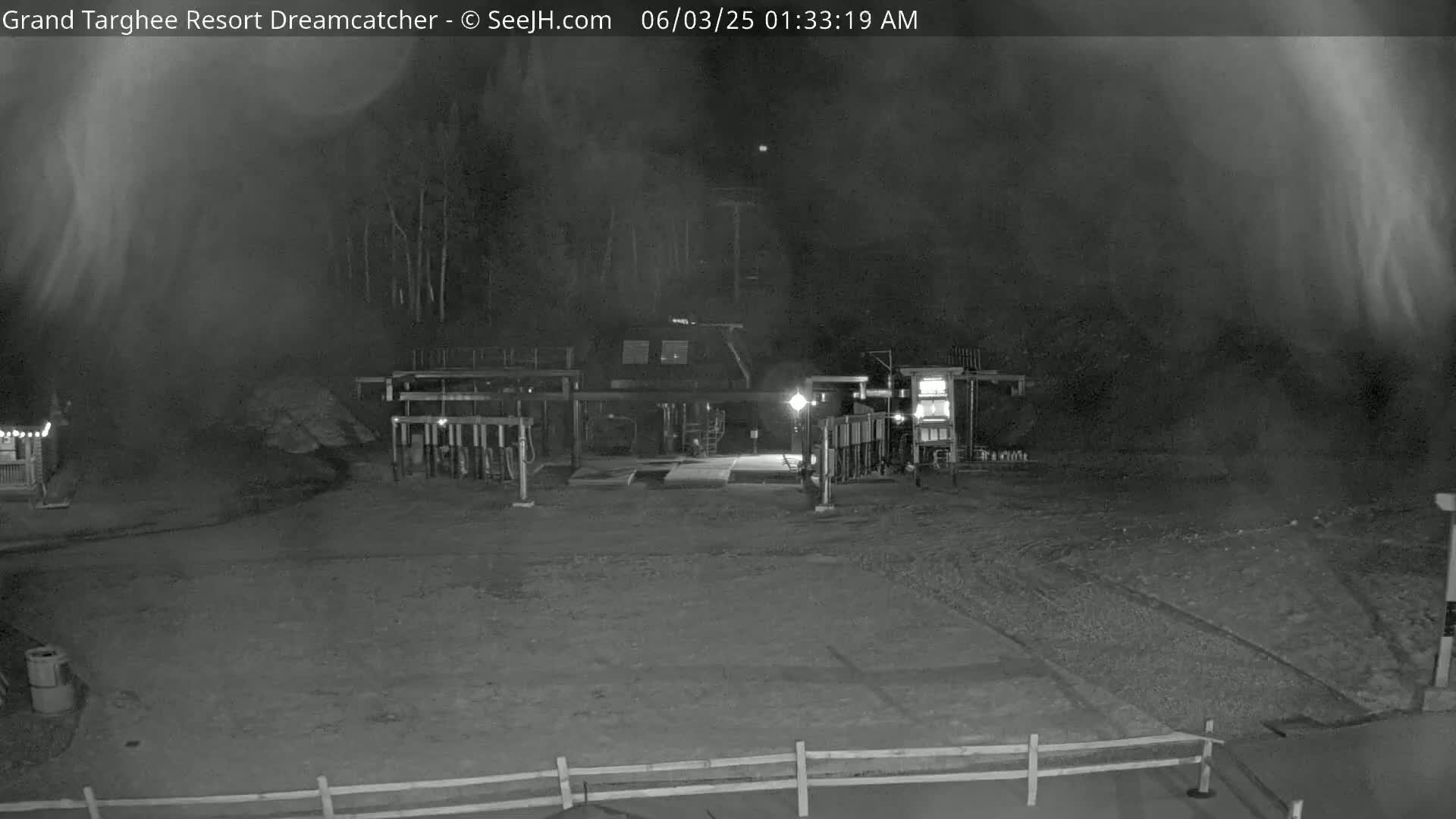 A nighttime, foggy view of an industrial area with a building and equipment, dimly lit by artificial lights.