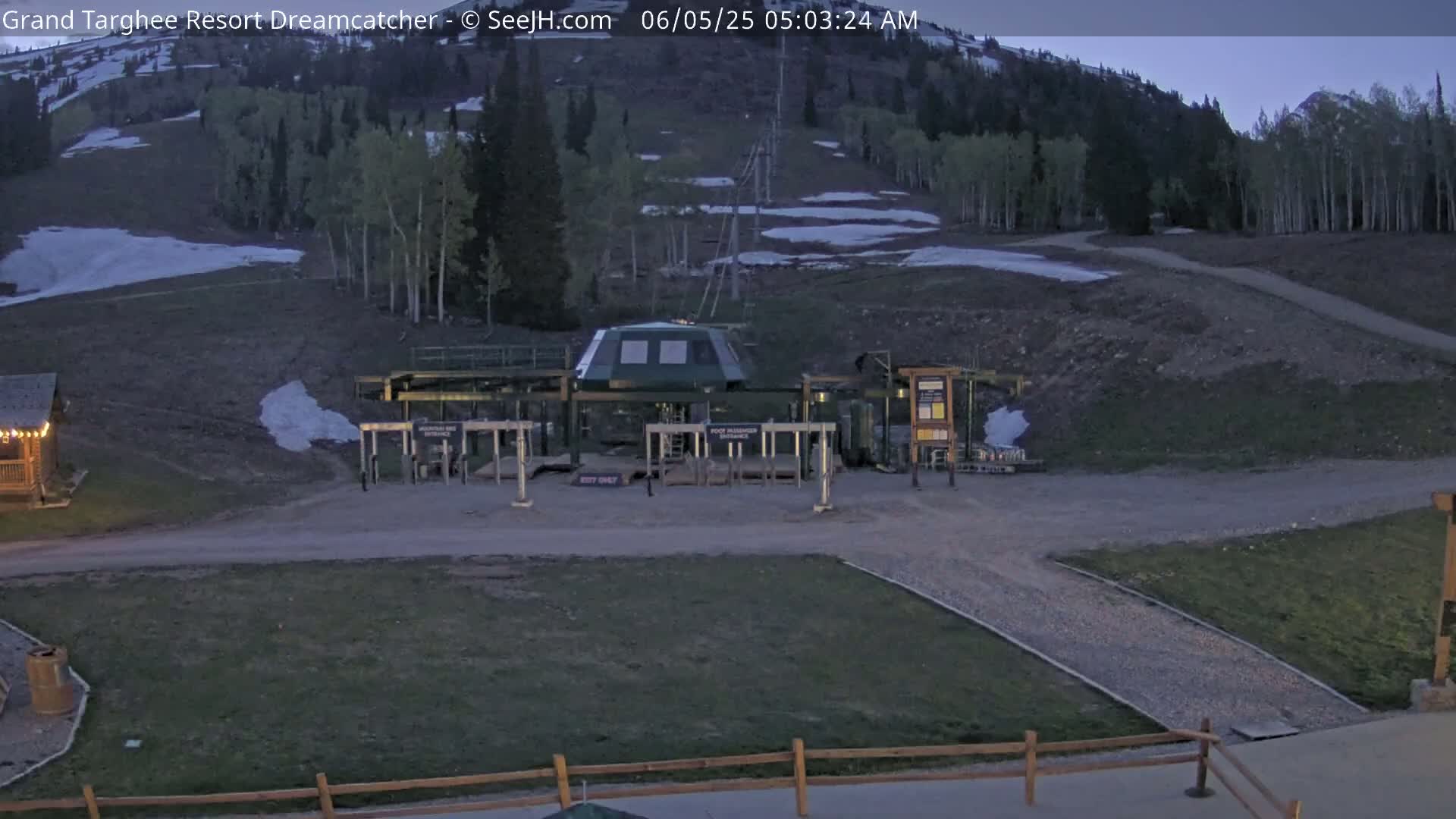 A ski lift base station sits at the bottom of a hill with patchy snow and early morning light.