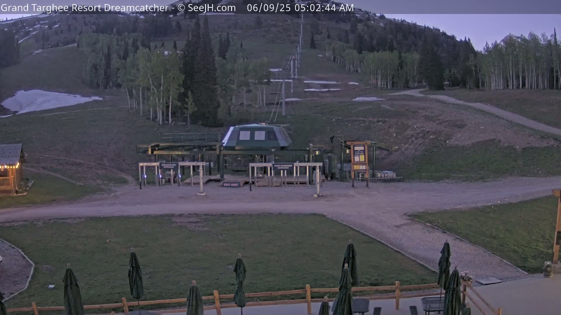 A ski lift base station sits at the bottom of a grassy hill under a twilight sky, with a small amount of snow visible in the background.