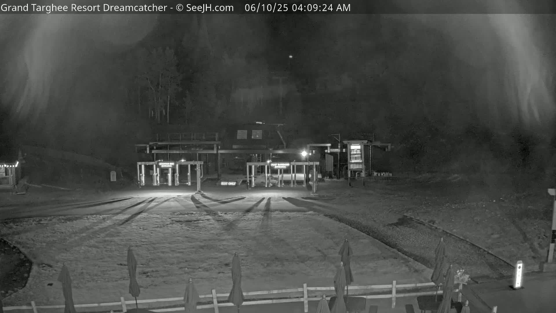 A nighttime, snow-covered parking lot with closed gates and several closed umbrellas is visible under a hazy sky.