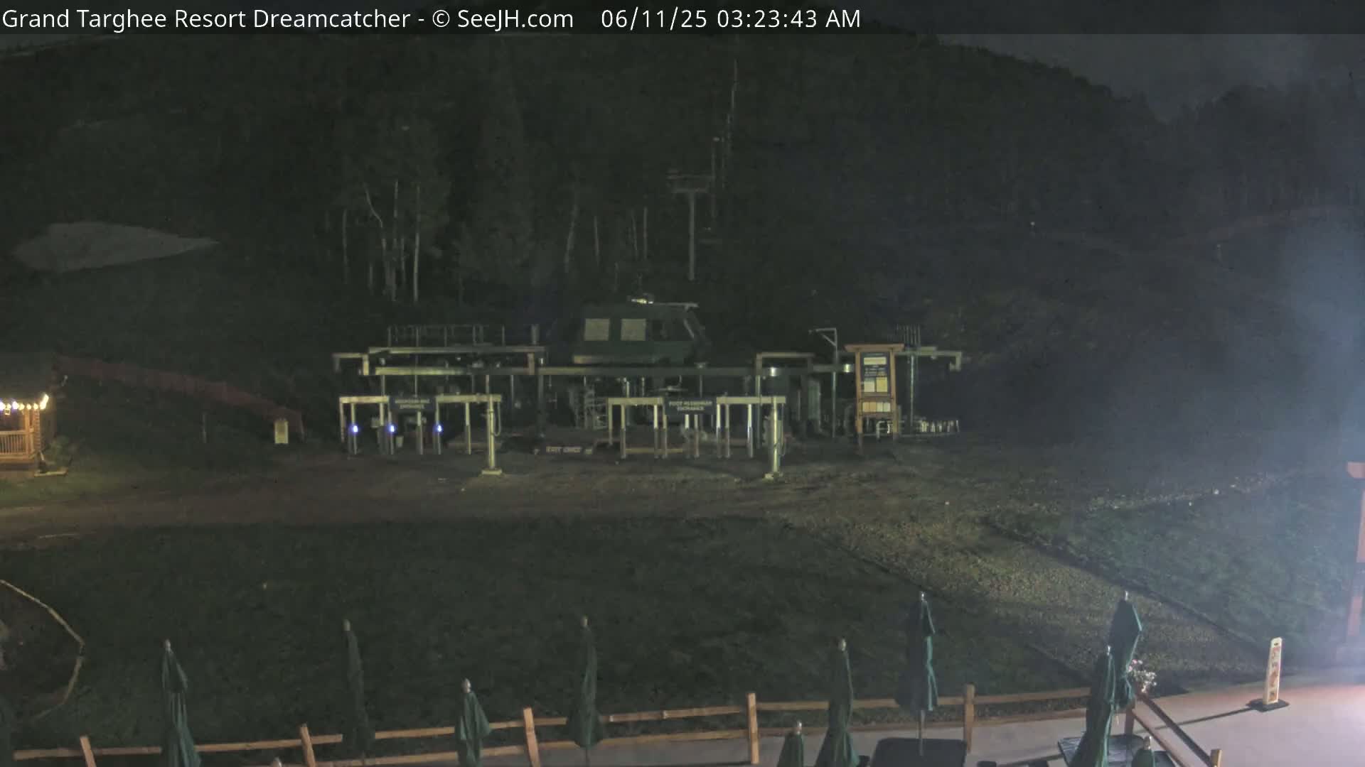 A nighttime view of a ski lift station with closed gates,  surrounded by dark vegetation and a few closed umbrellas.