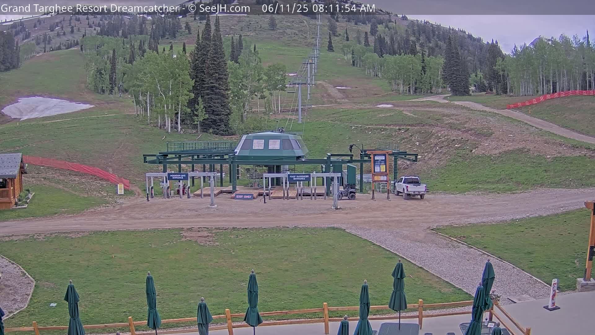 A ski lift base station sits in a grassy area at the base of a mountain on a partly cloudy day.