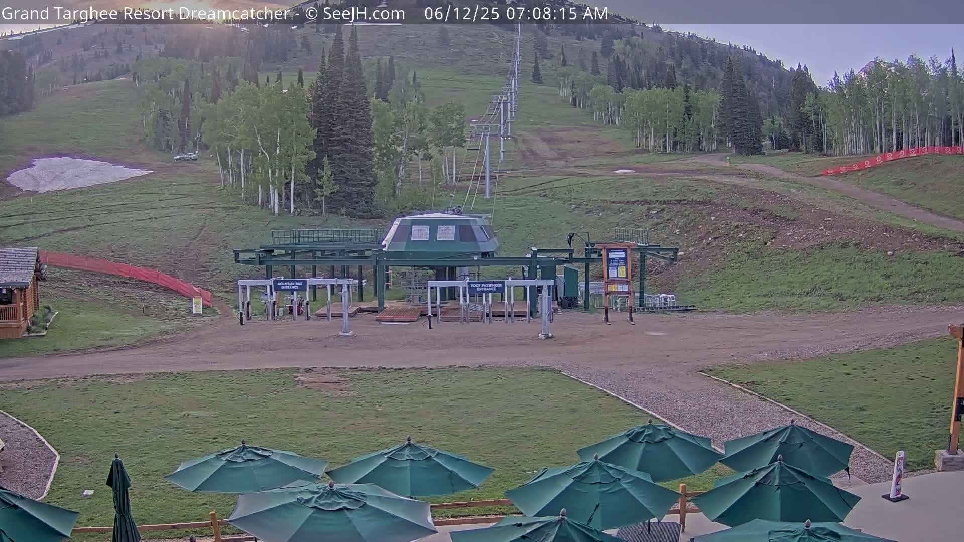 A ski lift base station sits in a grassy area with several dark green umbrellas in the foreground, under a mostly clear sky.