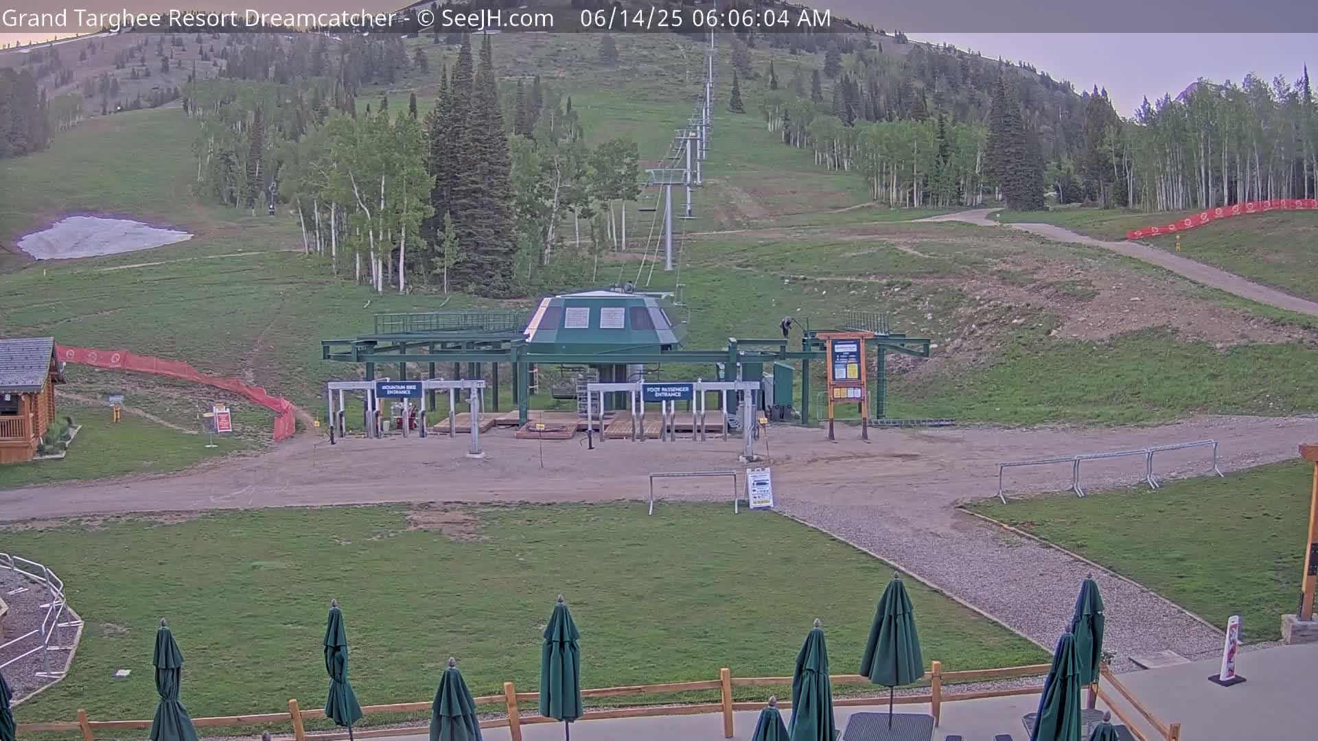 A ski lift base station sits on a grassy area near a mountainside, under a partly cloudy sky.