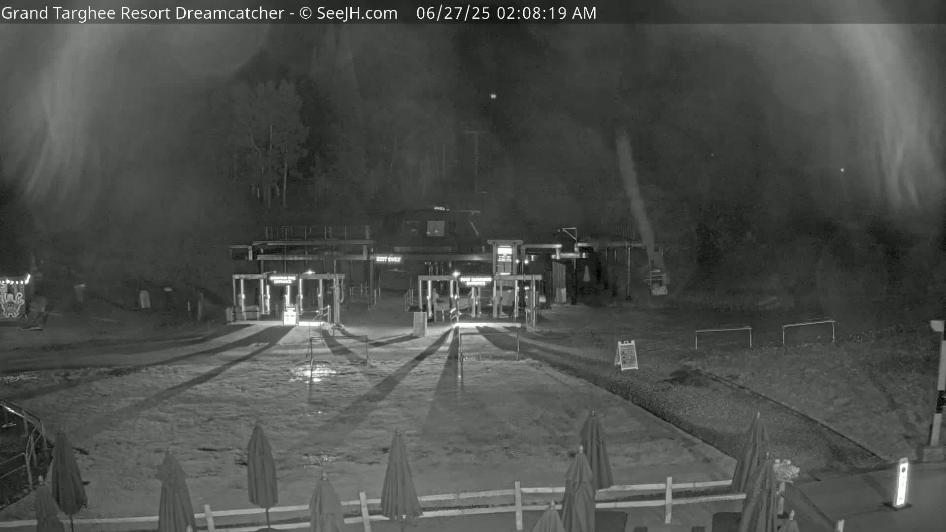 A nighttime, snowy scene shows a resort entrance with closed gates and several closed umbrellas in the foreground.