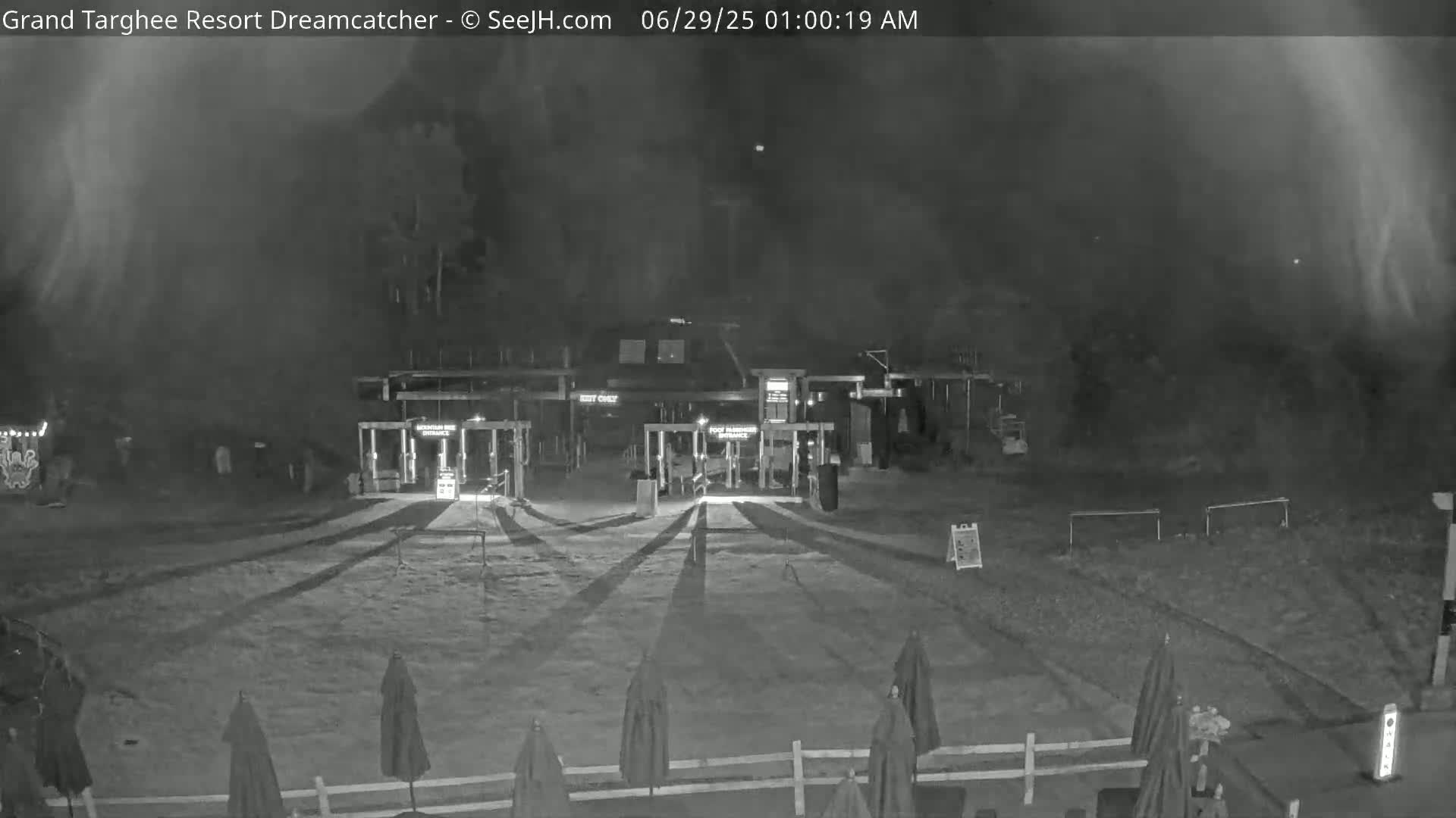 A nighttime, hazy view of a closed gate and a building, with several closed umbrellas in the foreground.