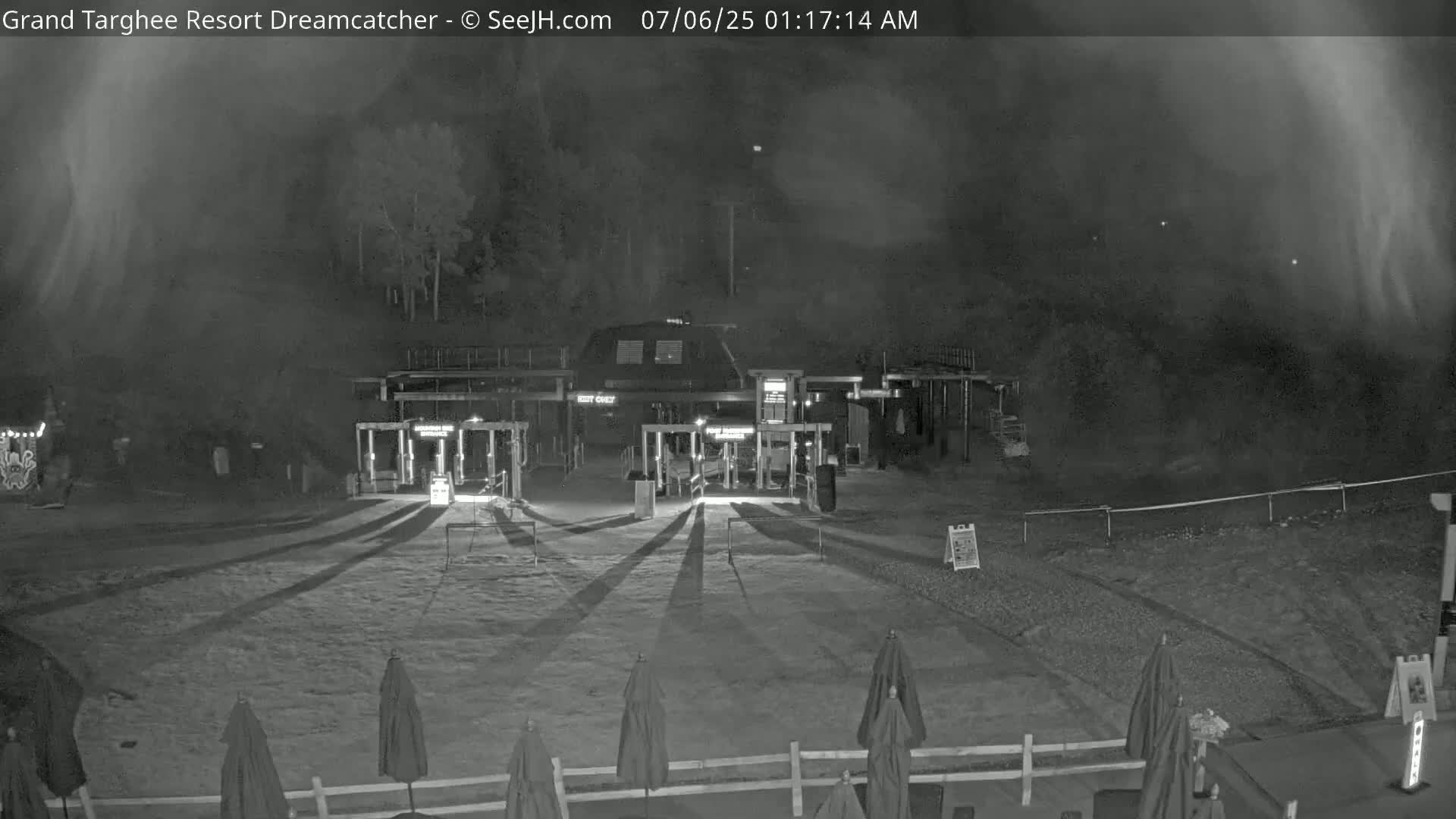 A nighttime, foggy view of a gated entrance to a building with several closed umbrellas in the foreground.