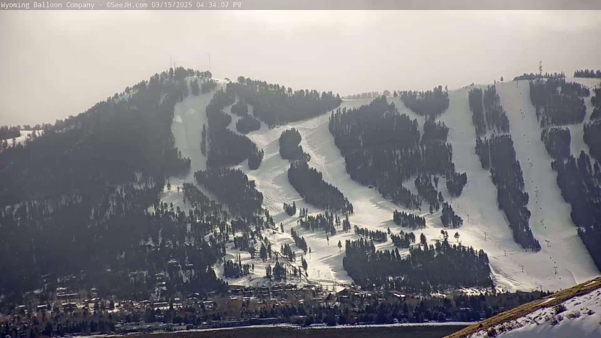 A snow-covered mountain with ski runs is visible, under hazy, bright conditions, with a town situated at its base.