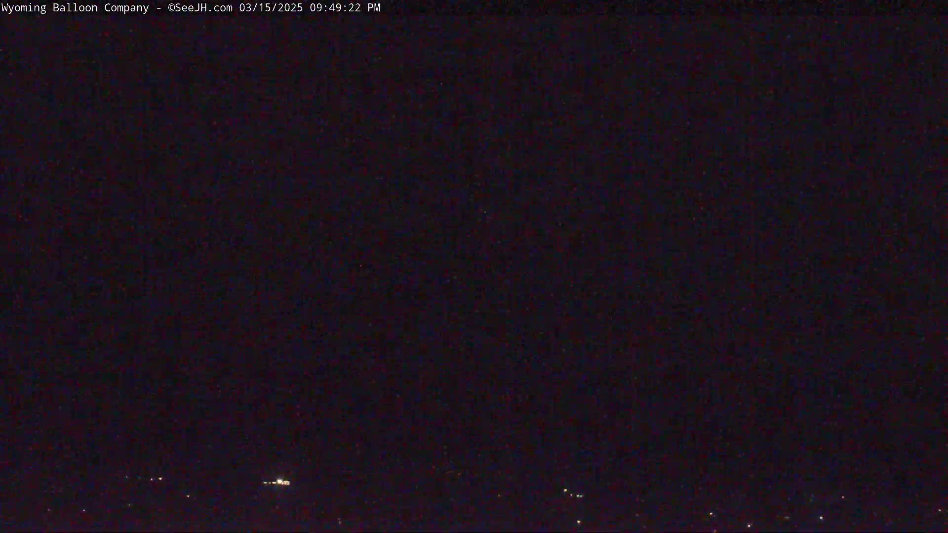 A nighttime, dark outdoor scene shows a few distant lights on the horizon under a clear, starlit sky.