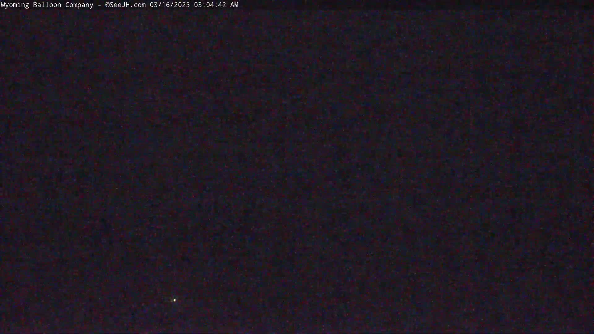 A dark, nighttime scene shows a single, faint light in the distance under a clear, starless sky.