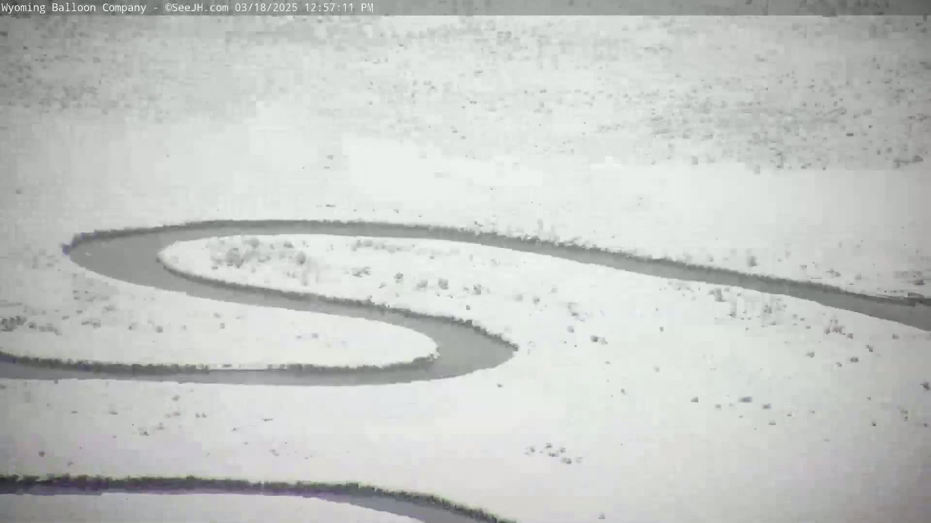 A winding dark river or stream meanders through a snow-covered landscape.